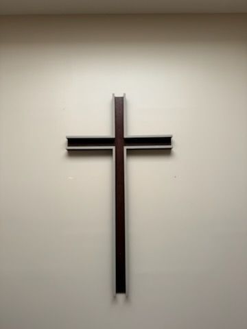 Wooden cross on a light-colored wall, lit from above.