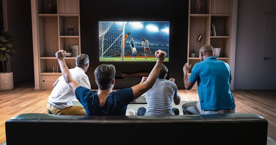 Group of men are sitting on a couch watching a soccer game