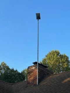 A brick chimney on top of a roof with a satellite dish pole attached to it