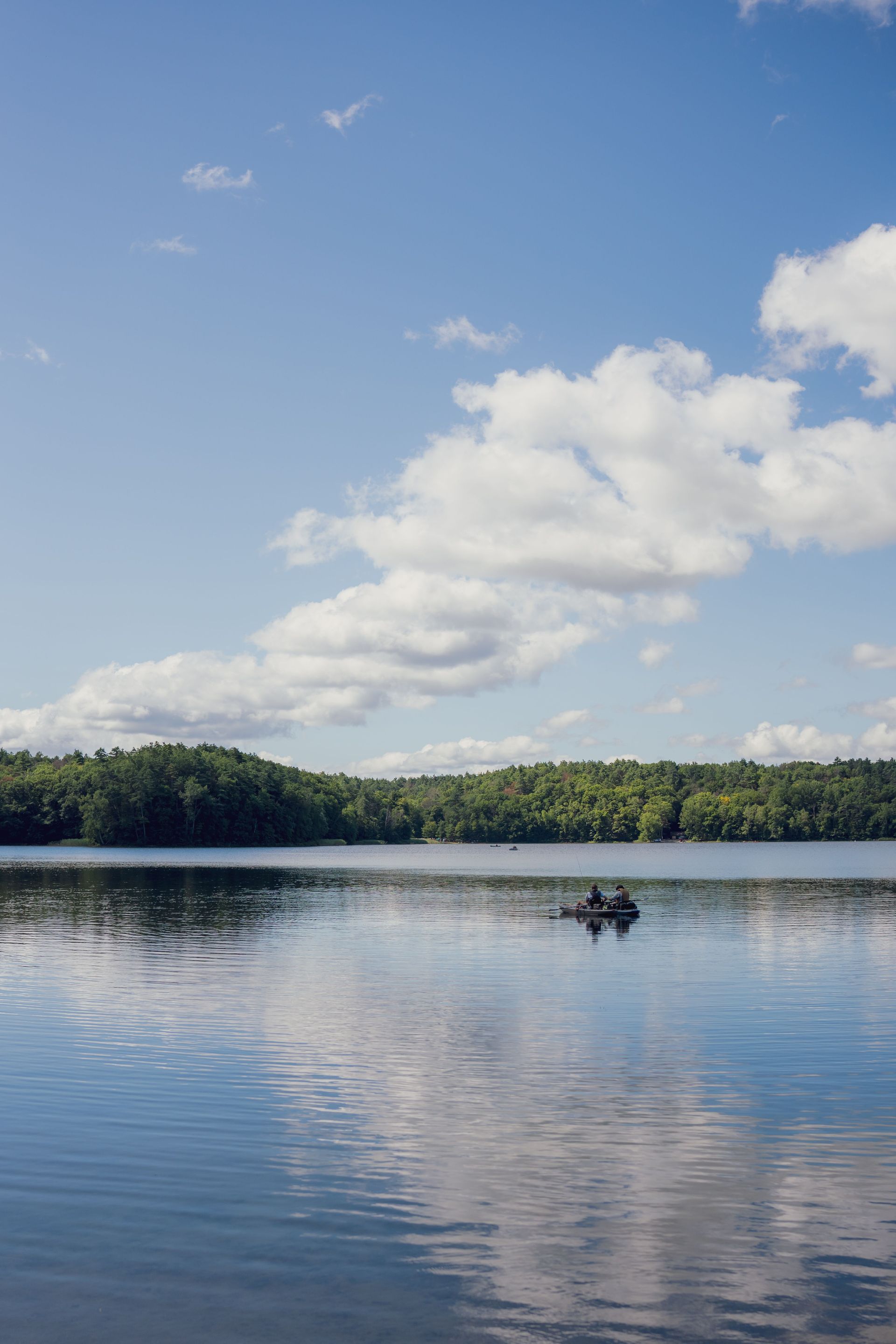 Calm lake reflecting clouds and blue sky, with a small boat near a forested shore