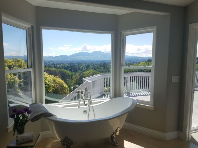 Bathroom with a white clawfoot tub overlooking a mountain and forest view through large bay windows