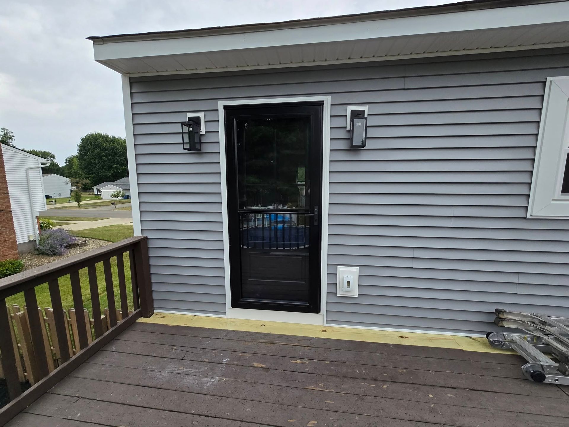 Black screen door on gray sided building, flanked by sconces. Brown deck in foreground.