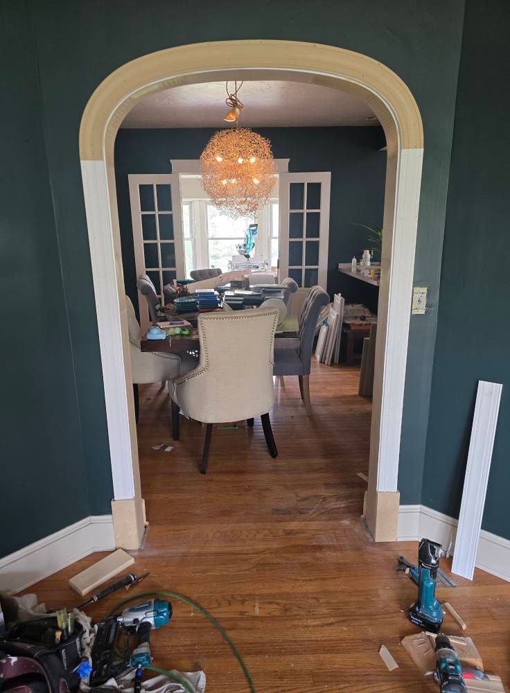 Arched doorway in a teal room, leading to a dining area. Work tools and trim pieces visible.