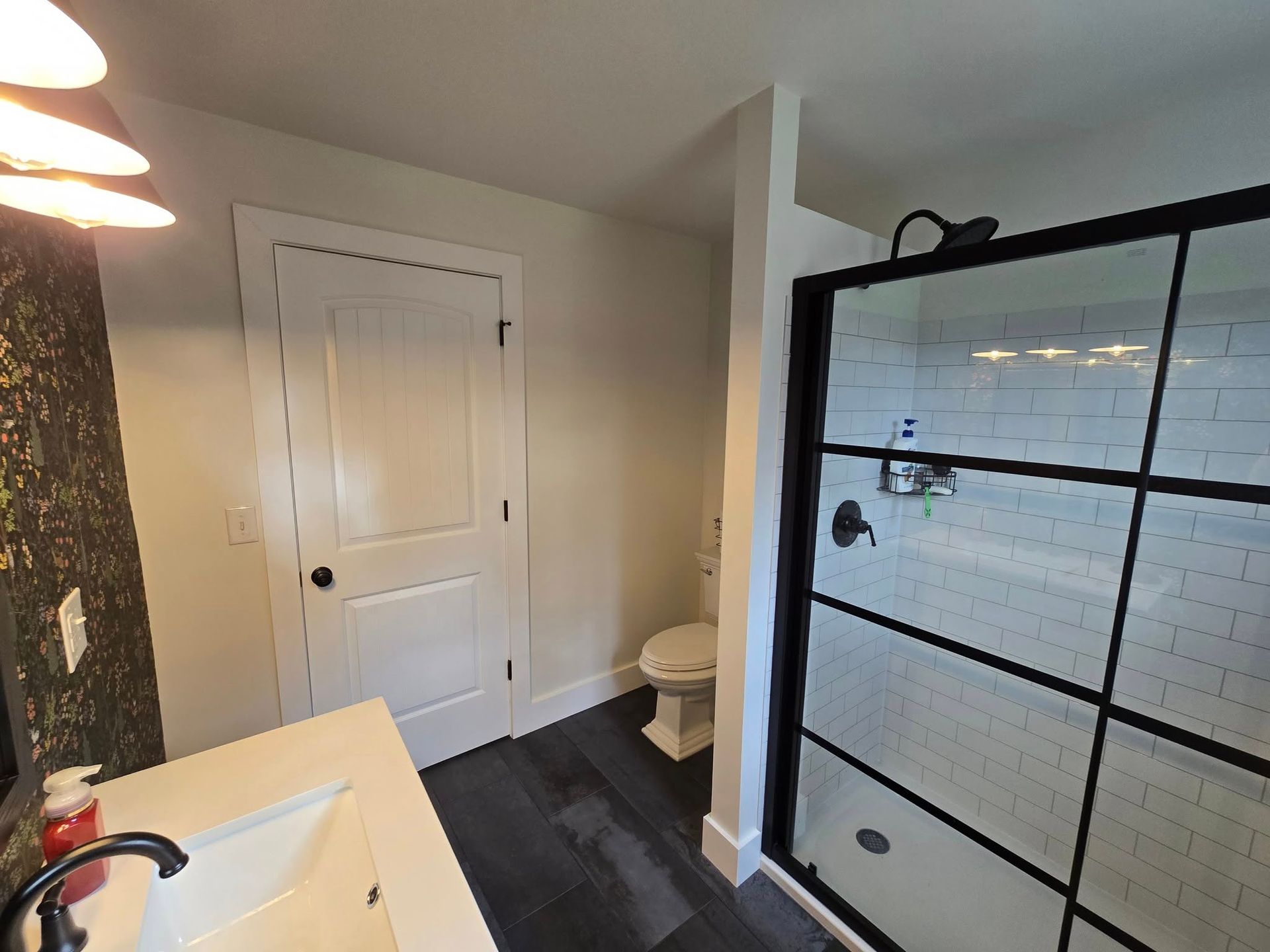 Bathroom with a black-framed shower, white sink, and dark wood flooring.