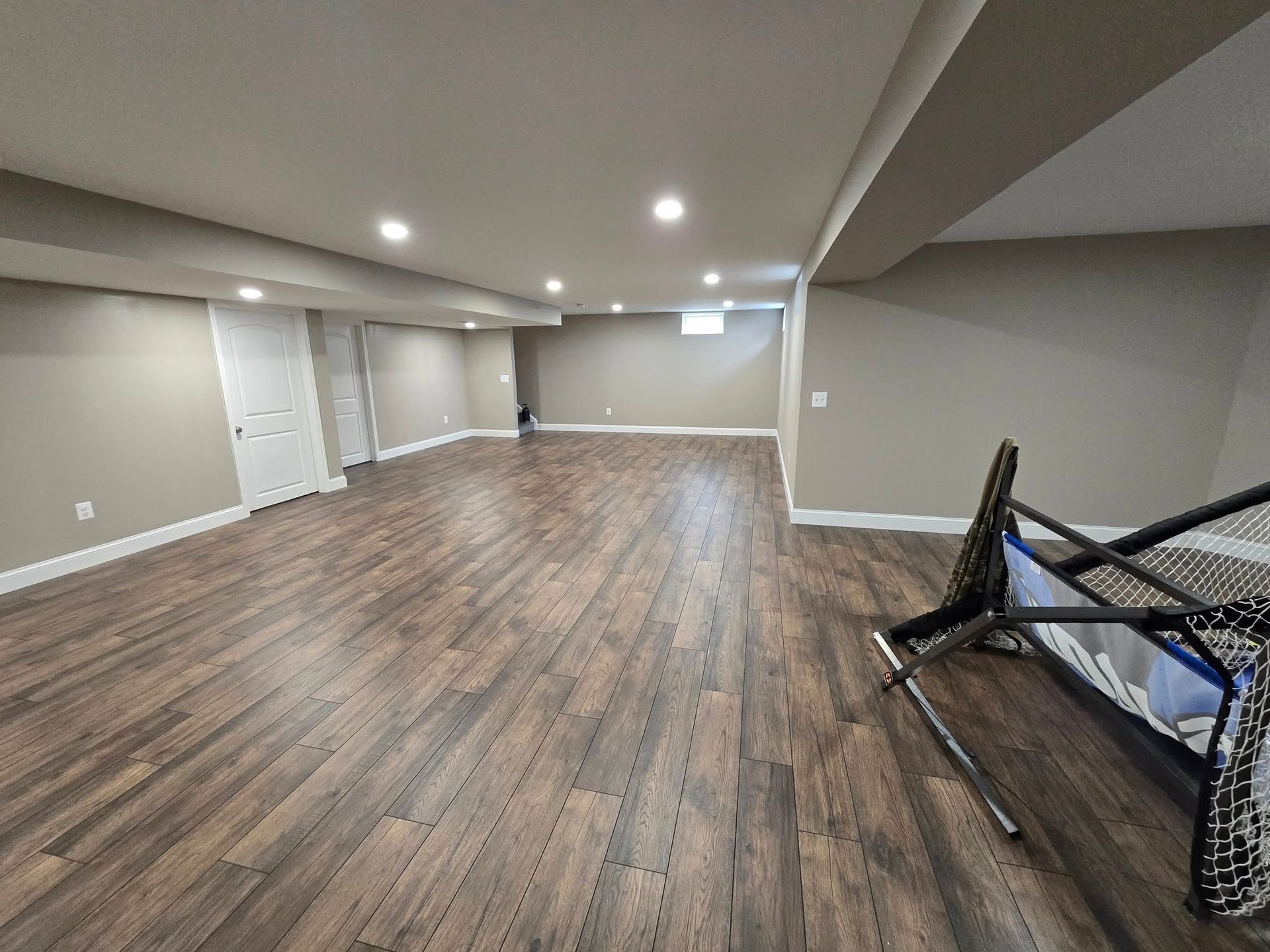Empty basement room with wood-look flooring, light gray walls, recessed lighting, and a soccer net.