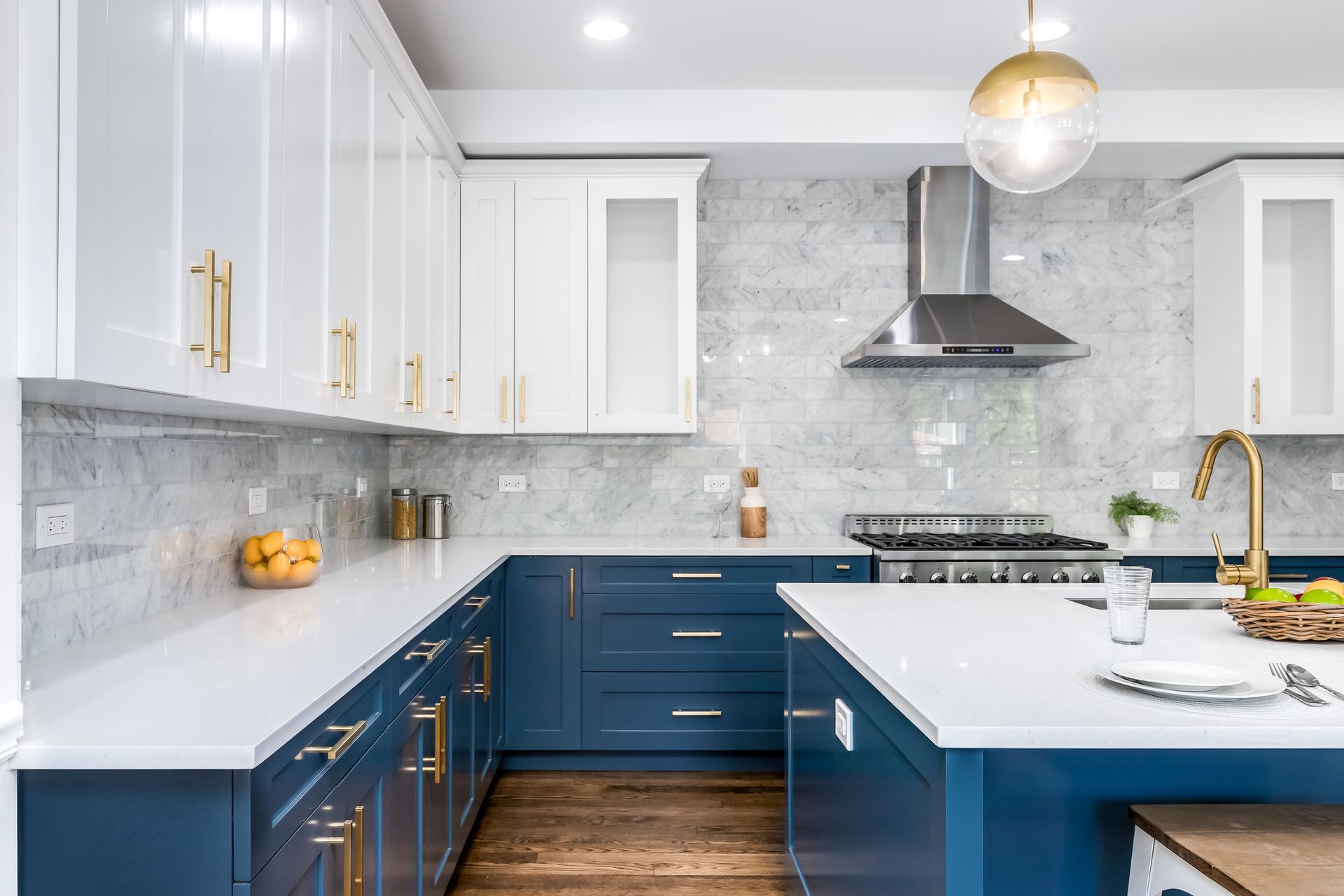 Modern kitchen with white and navy blue cabinets, marble backsplash, gold hardware, and island.