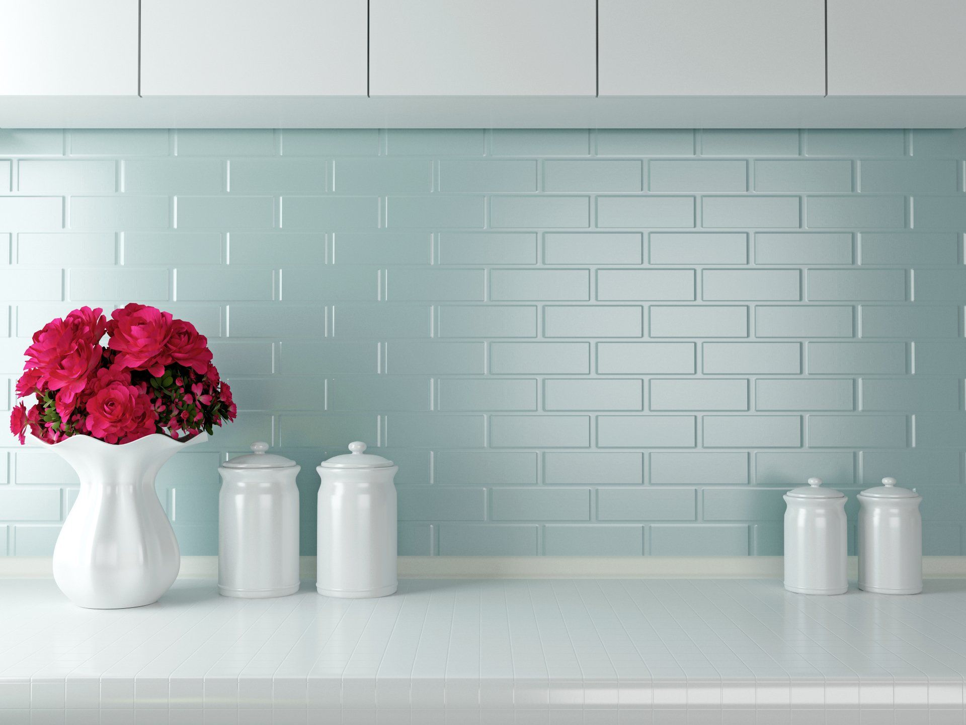 Red flowers in white vase on a white countertop, with white canisters, and turquoise brick-pattern backsplash.
