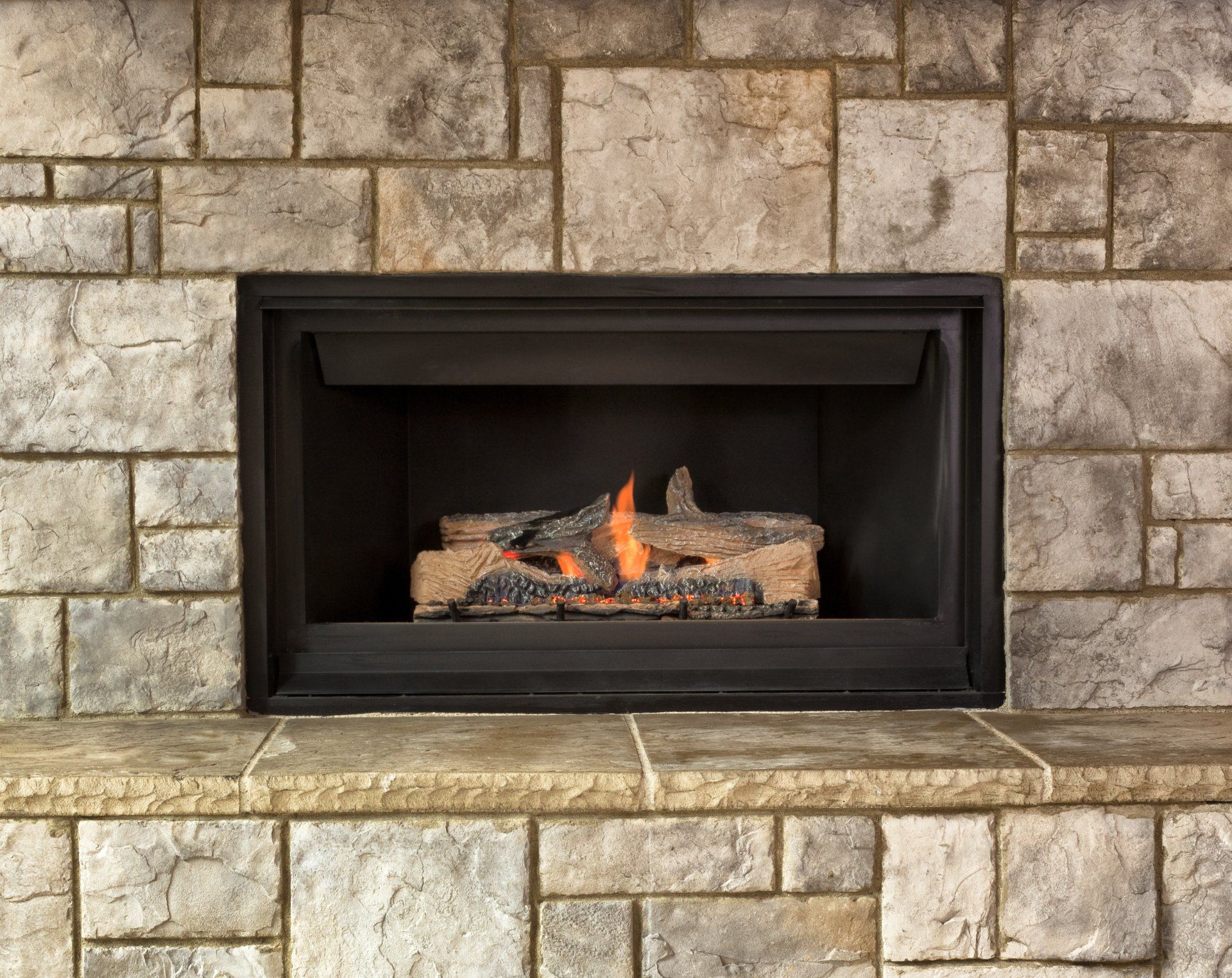 Fireplace with burning faux logs inside a black metal frame, set in a stone wall.