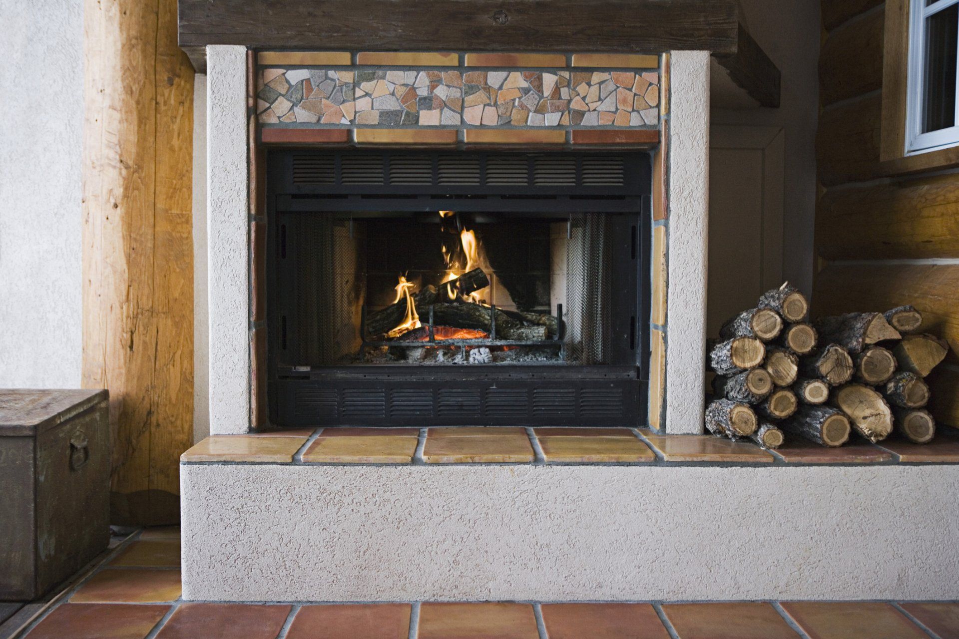 Fireplace with burning fire, stacked firewood, and brick-tiled hearth.