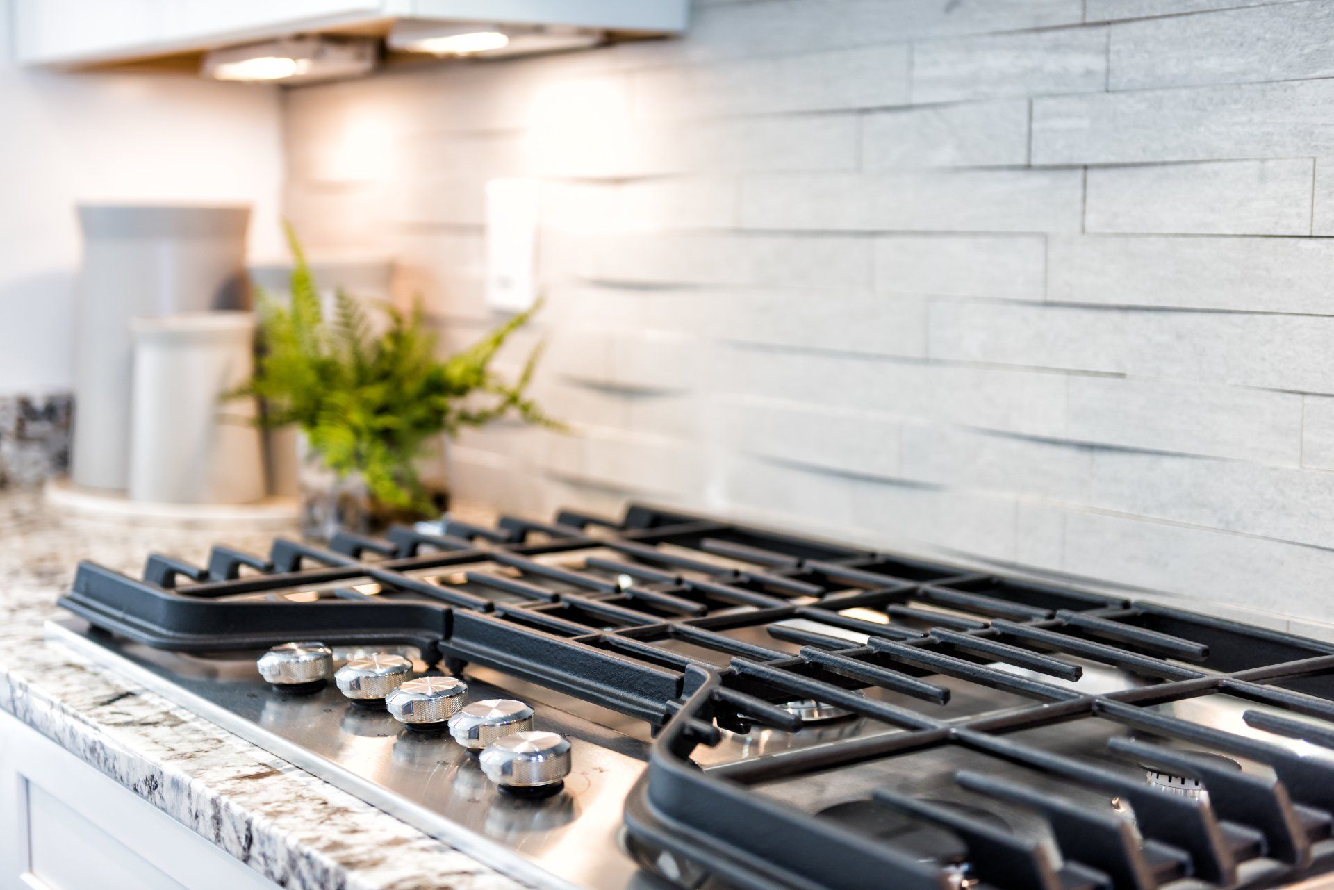 Gas stovetop with gray backsplash and granite countertop.