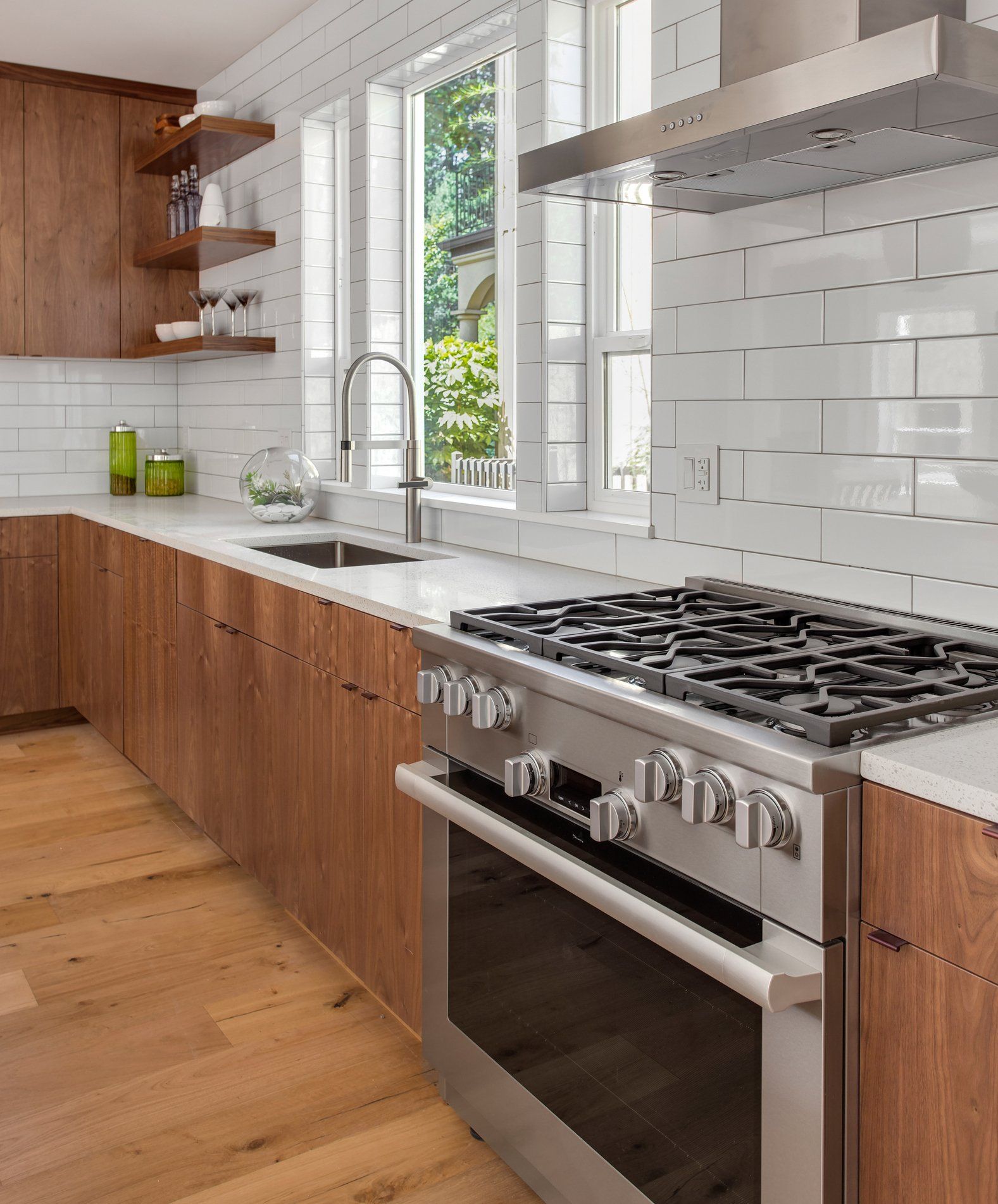 Modern kitchen with wood cabinets, stainless steel appliances, white tile backsplash, and a large window.
