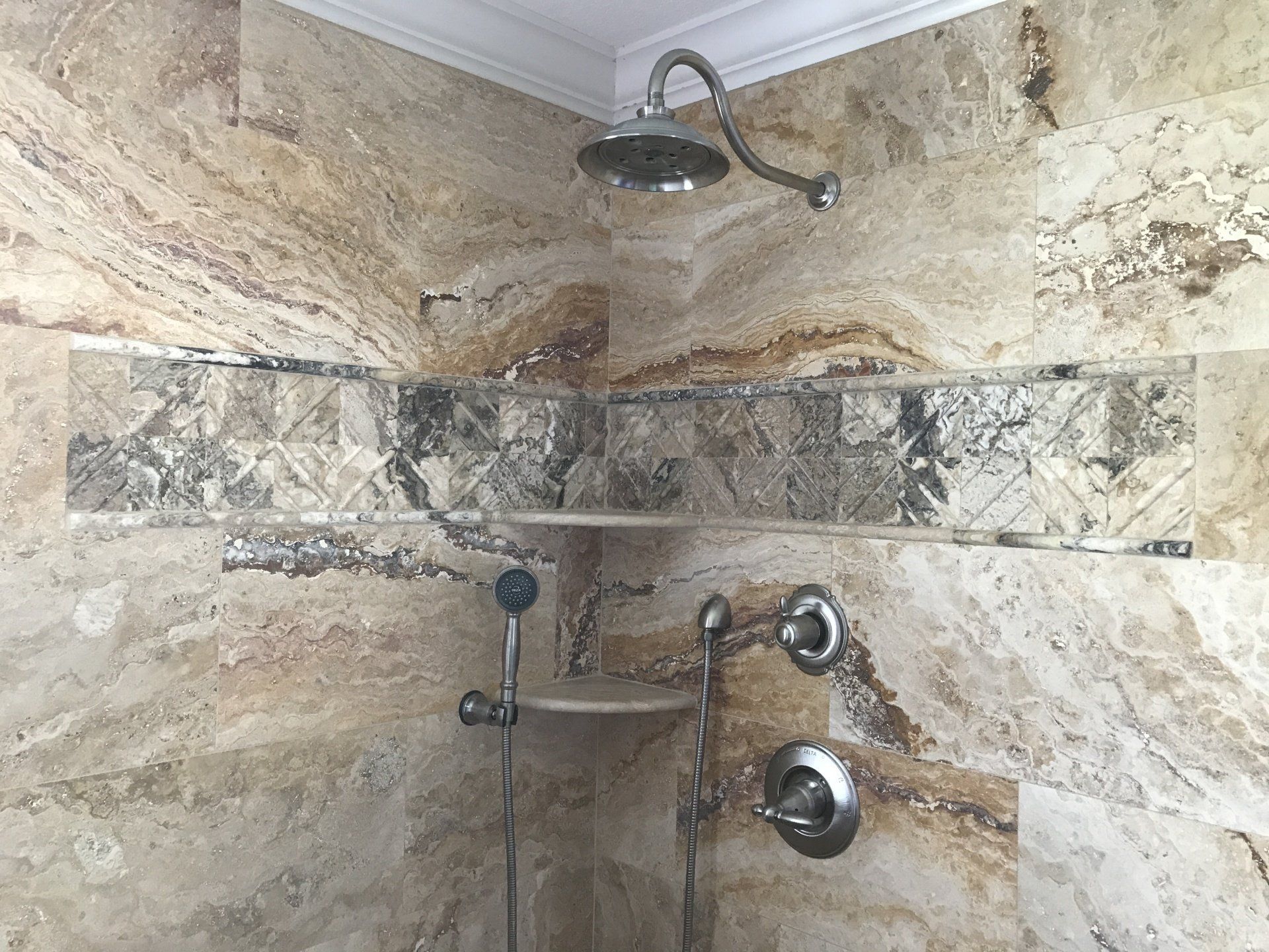 Shower with tan and brown patterned tiles, a decorative center strip, and silver fixtures.