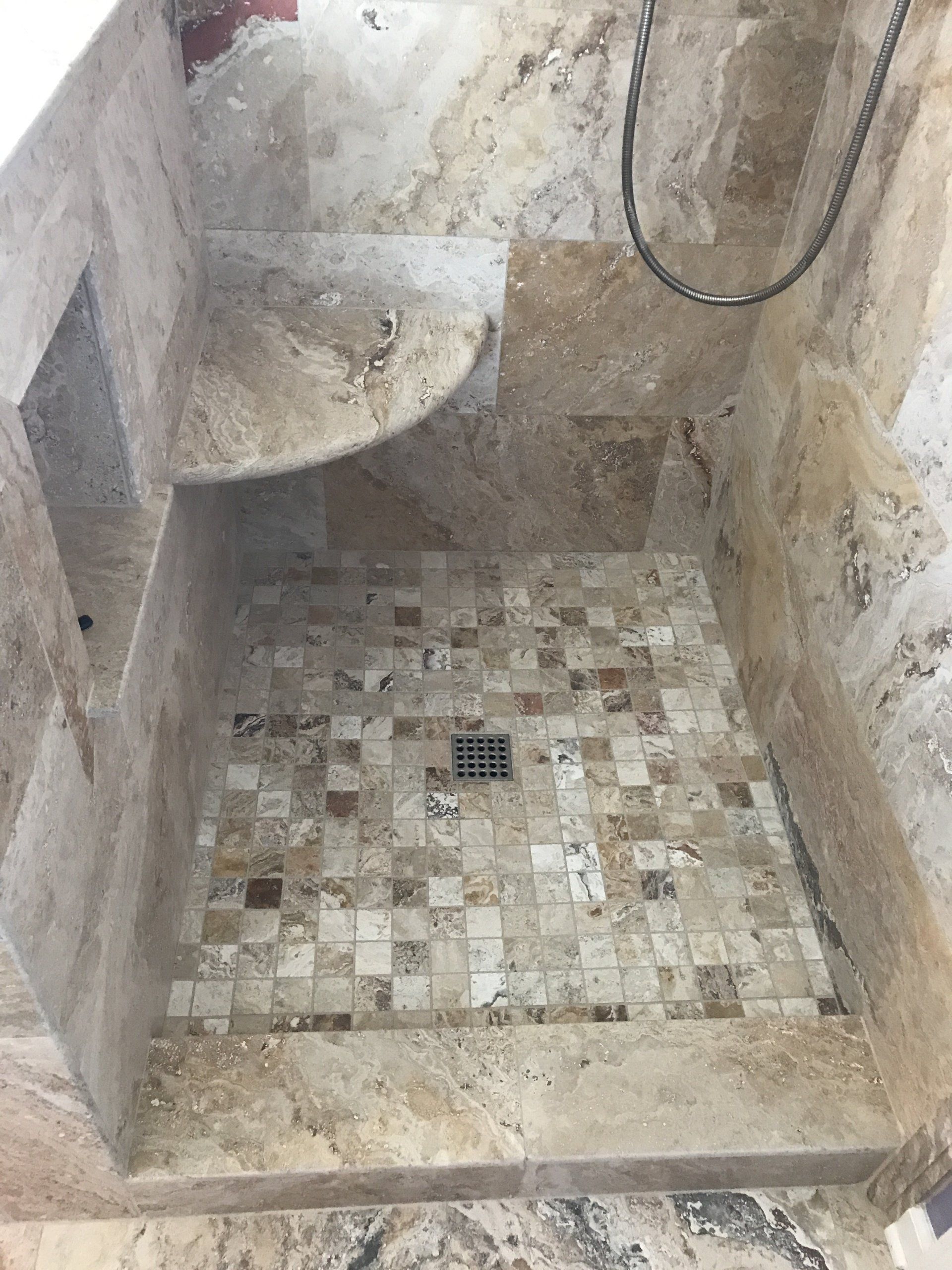 Stone tile shower with a built-in shelf and mosaic floor, featuring a metal drain.