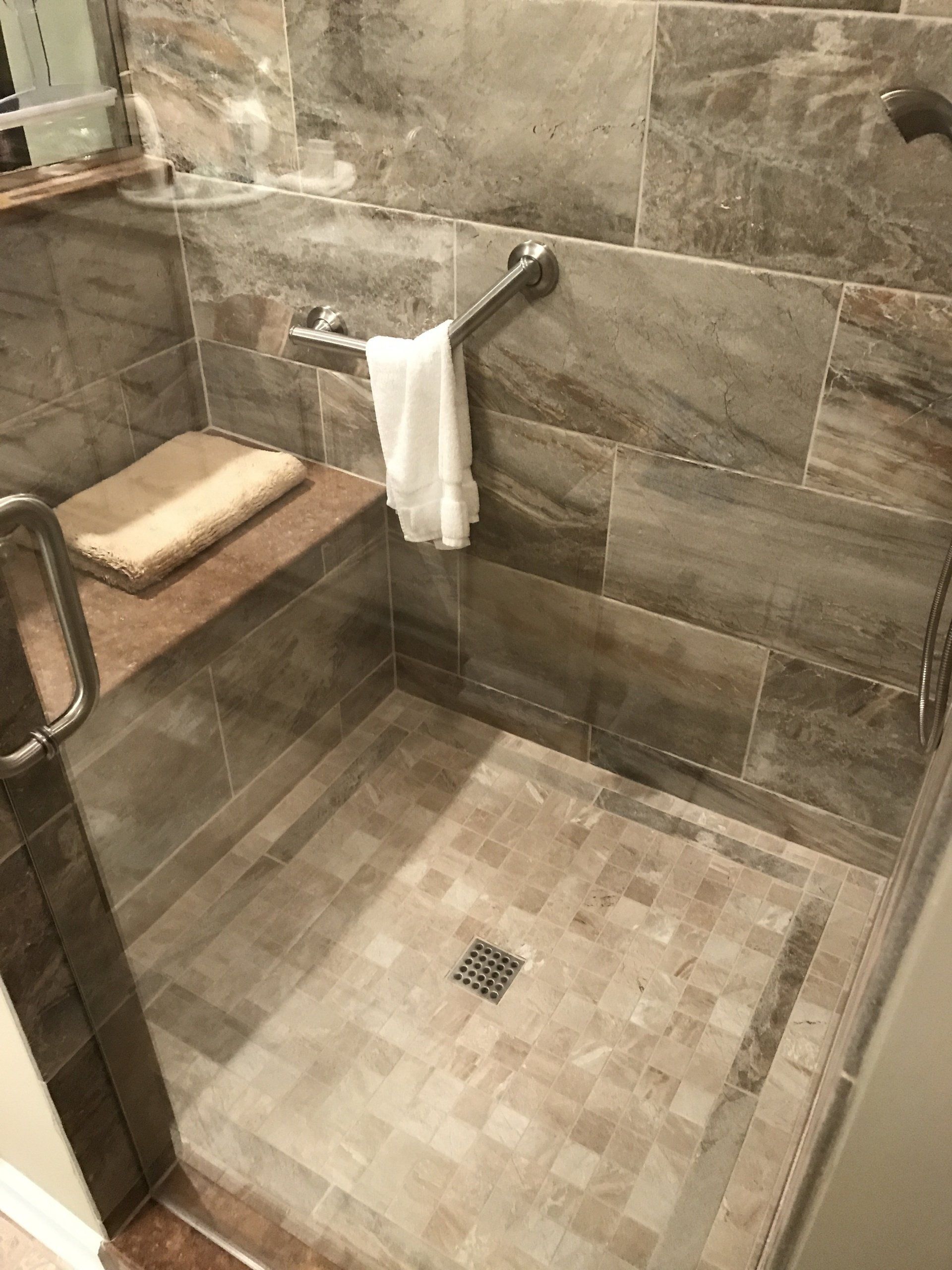 Accessible shower with grab bar, bench, and glass door. Beige and gray tile.