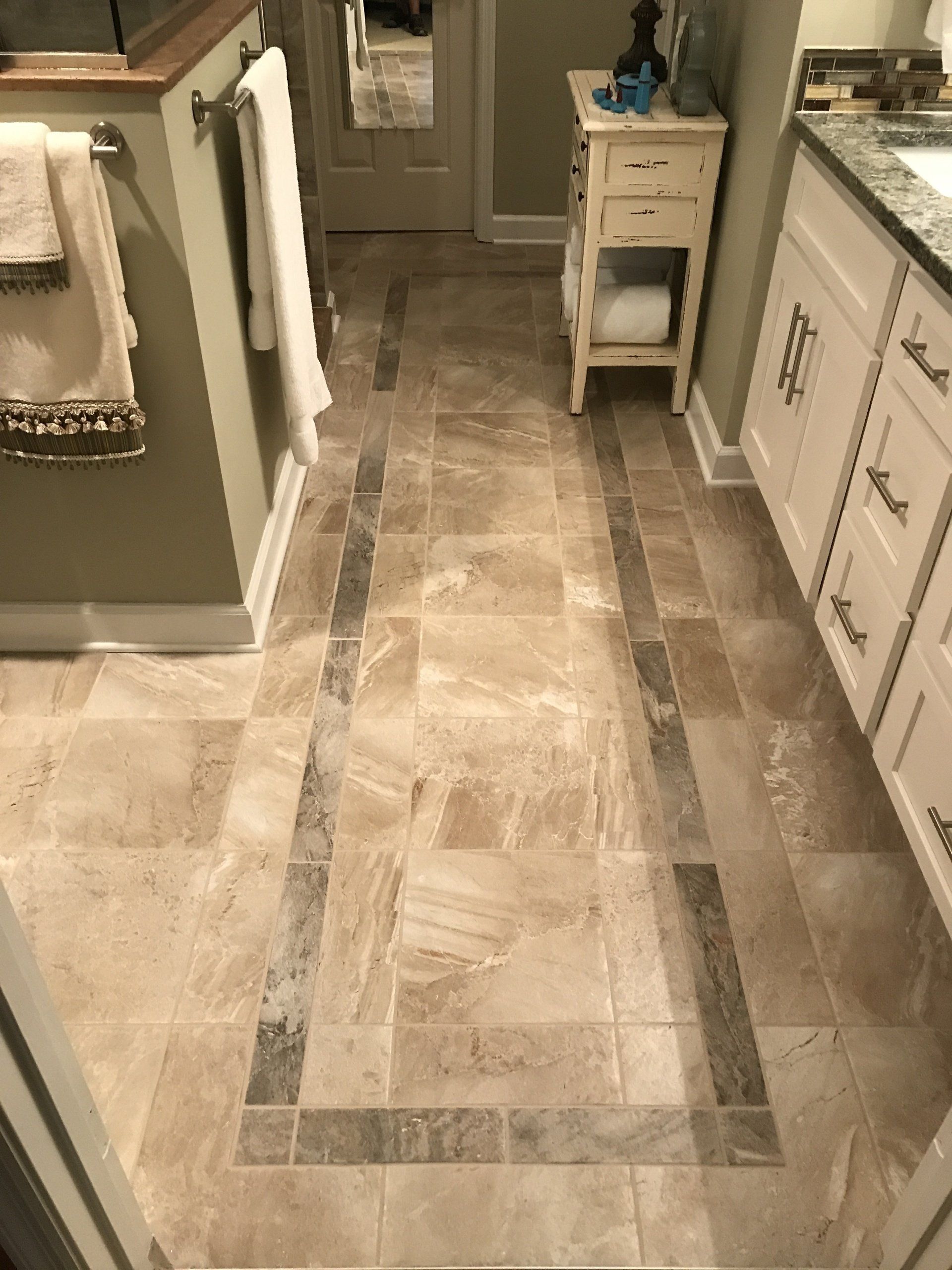 Bathroom with beige tile floor, marble accent strips, white vanity and cabinet, and small off-white side table.