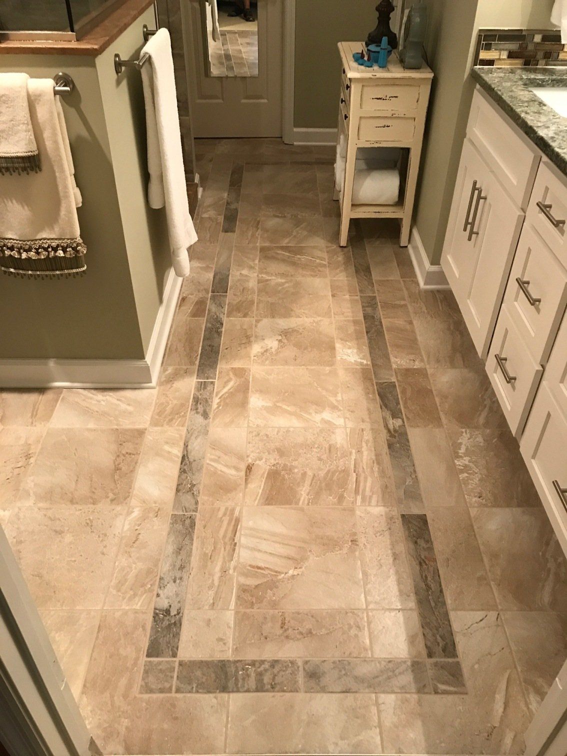 Bathroom floor with beige tiles and dark gray borders. A white vanity, sink, and small cabinet are visible.