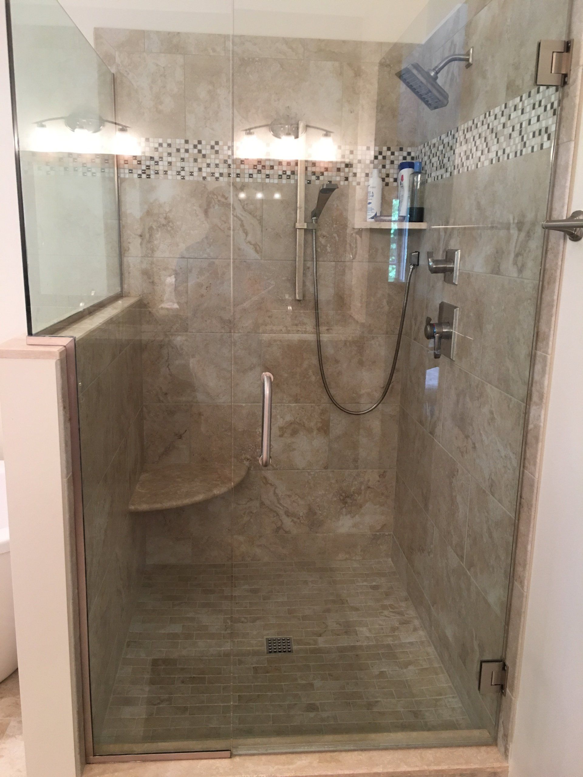 Glass-doored shower with tan tile walls, a built-in seat, and silver shower fixtures.