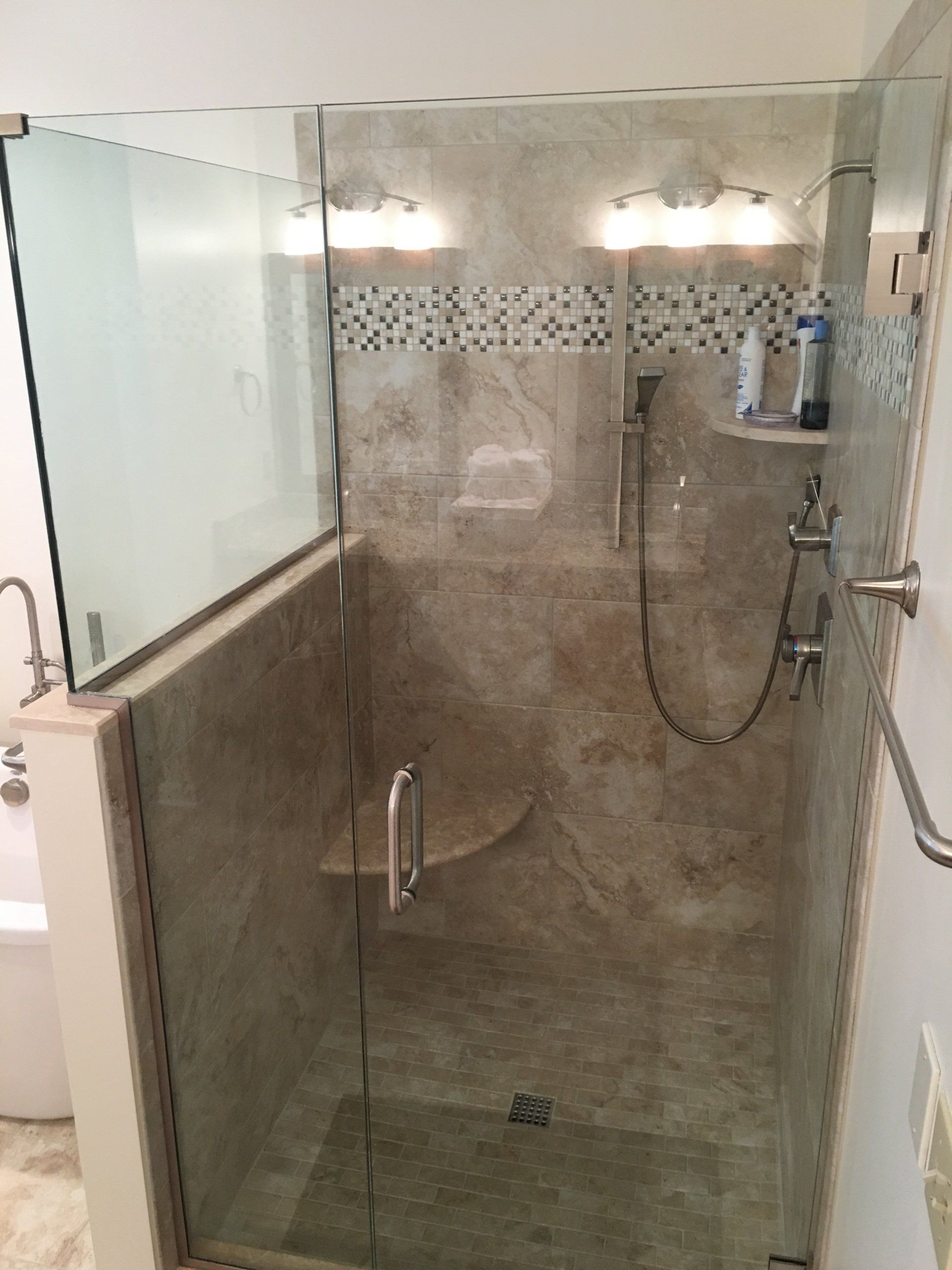Glass shower with stone tile walls, a built-in seat, and chrome fixtures.