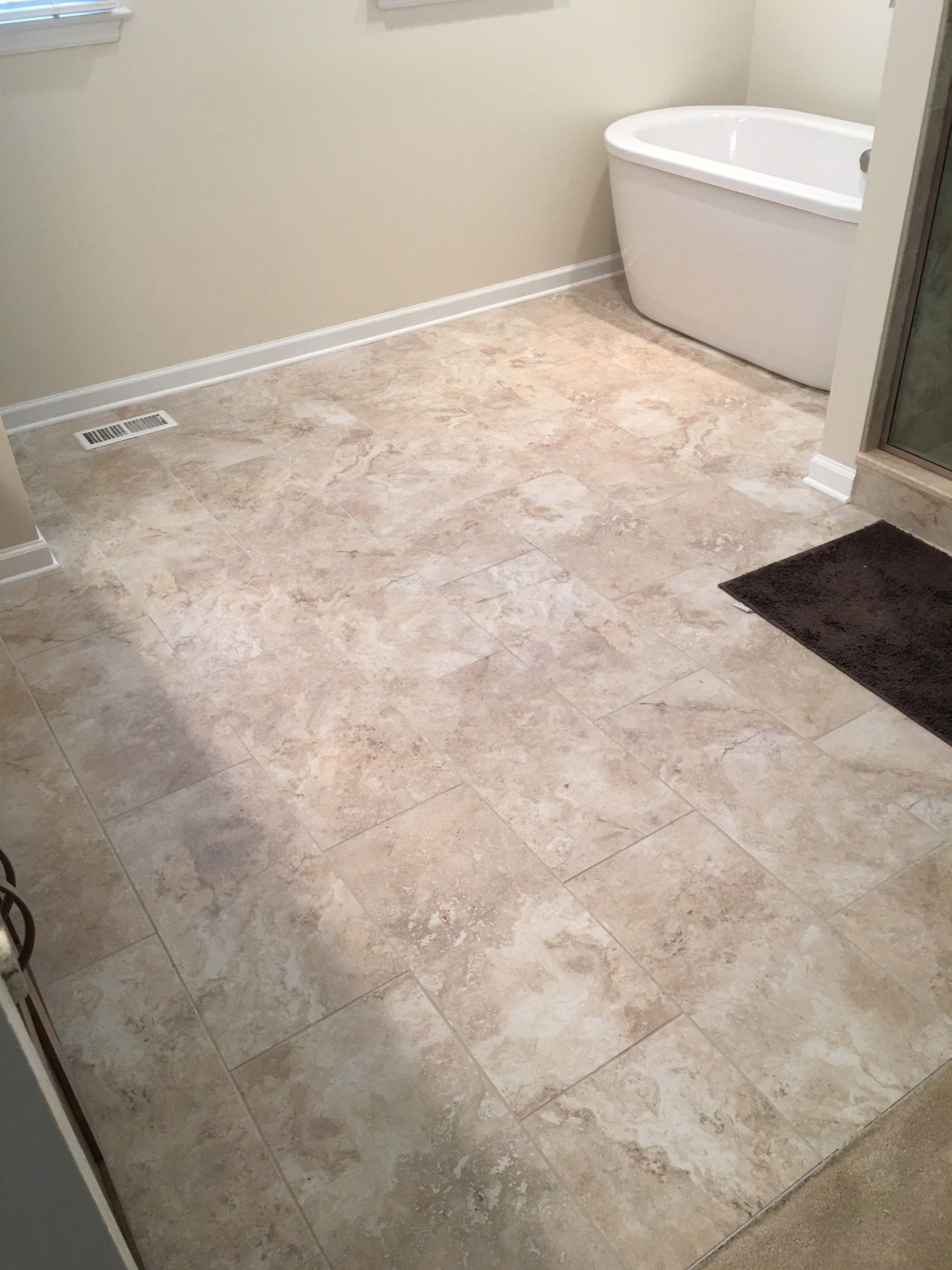 Bathroom with beige tiled floor, white tub, and tan walls.