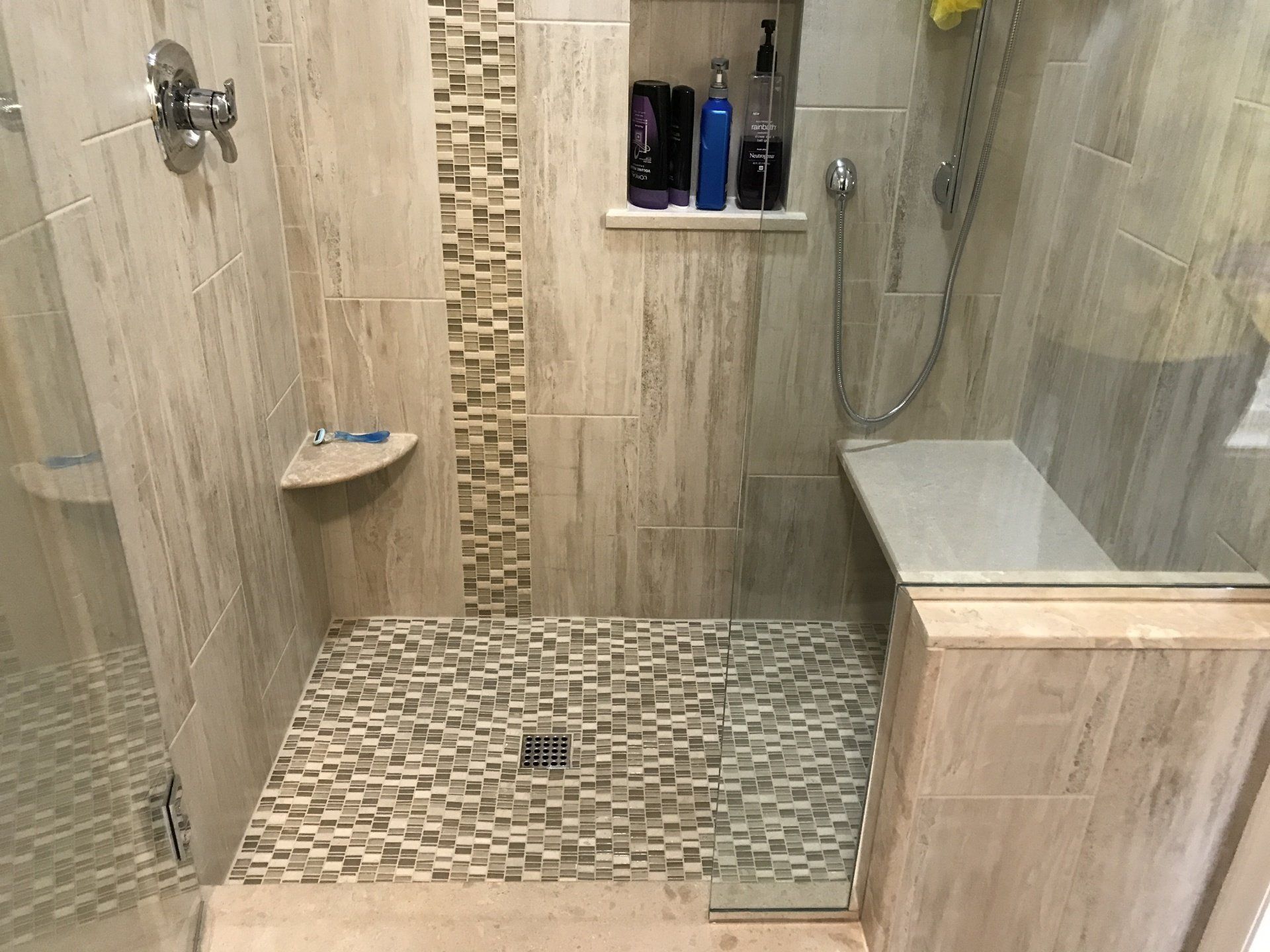 Shower with beige tile walls and mosaic tile floor, built-in bench, and shampoo niche.