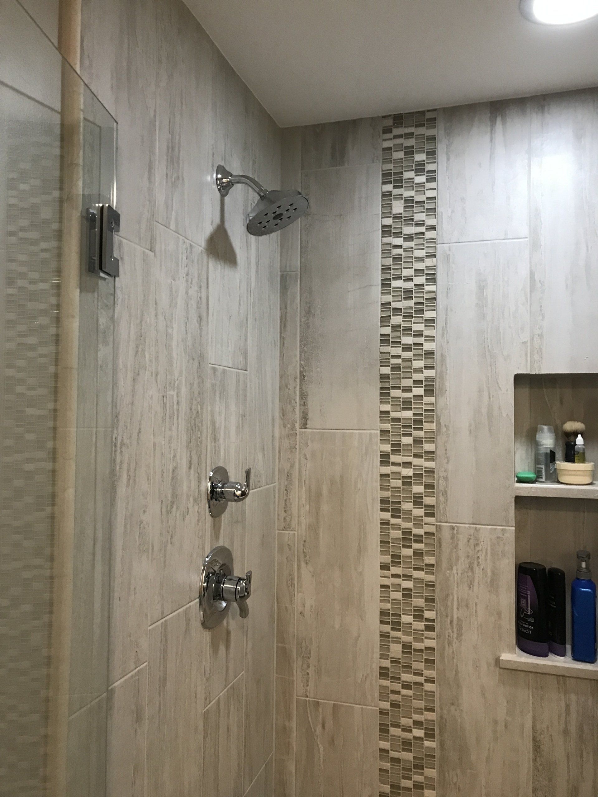 Shower with light gray tiles, a mosaic accent, and a built-in shelf with toiletries.