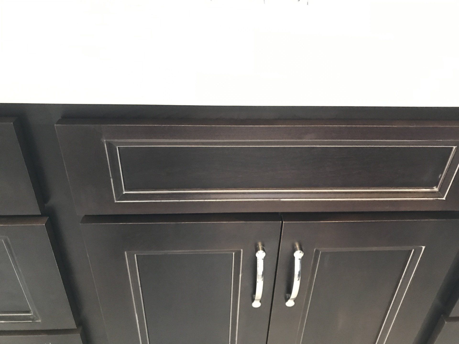 Dark brown kitchen cabinets with silver hardware and white countertop.
