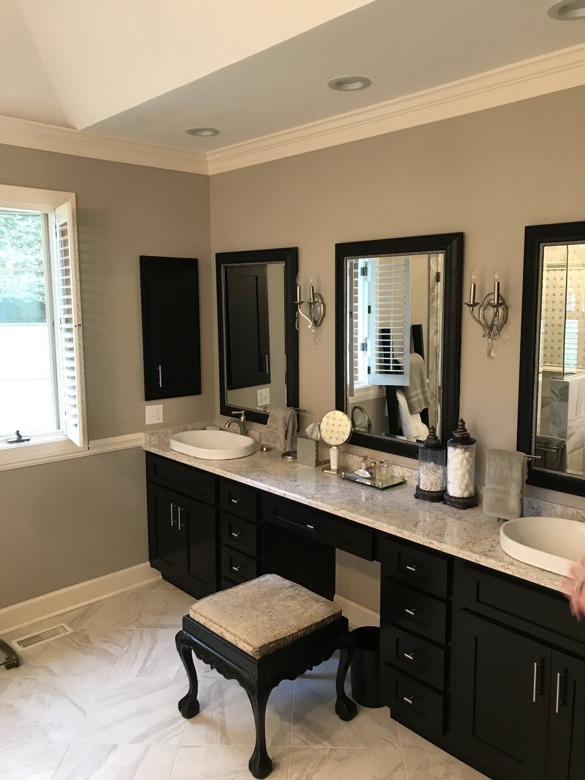 Bathroom with dark cabinets, marble countertop, three mirrors, and a stool.
