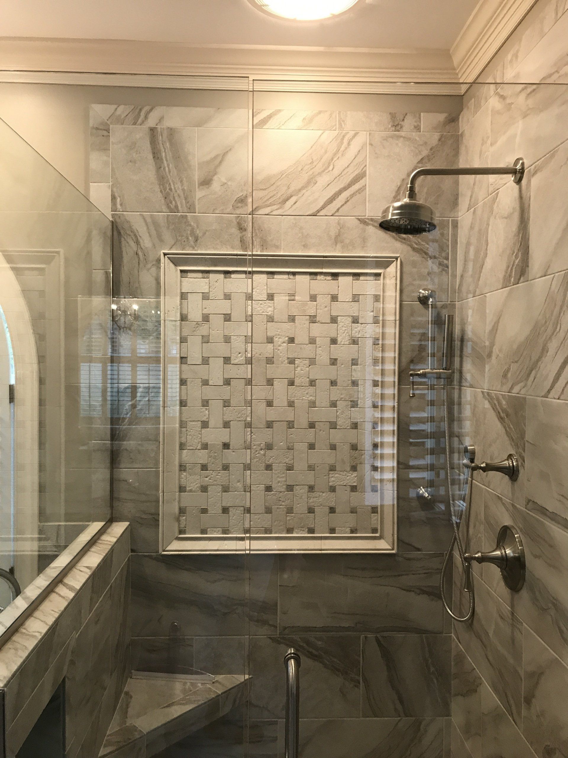 Shower with gray marble tiles, glass door, and a woven tile accent. Silver fixtures.