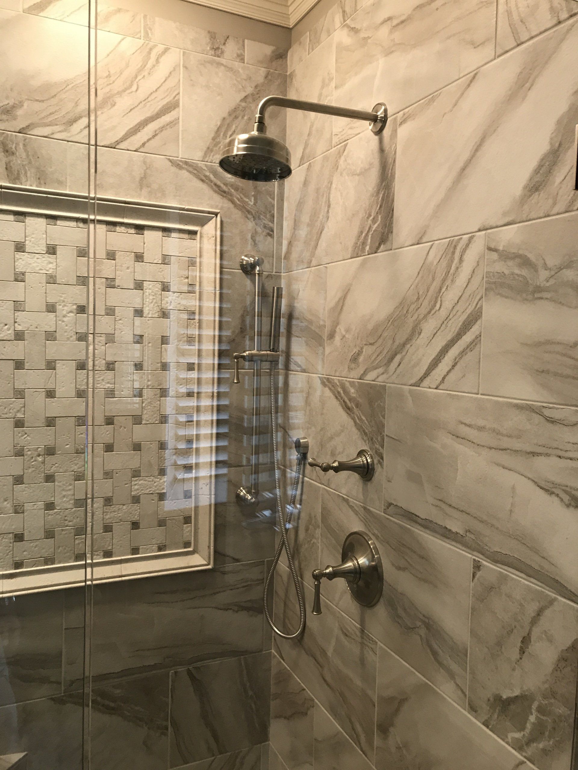 Shower with marble-like tiles, a rain showerhead, and a decorative niche.