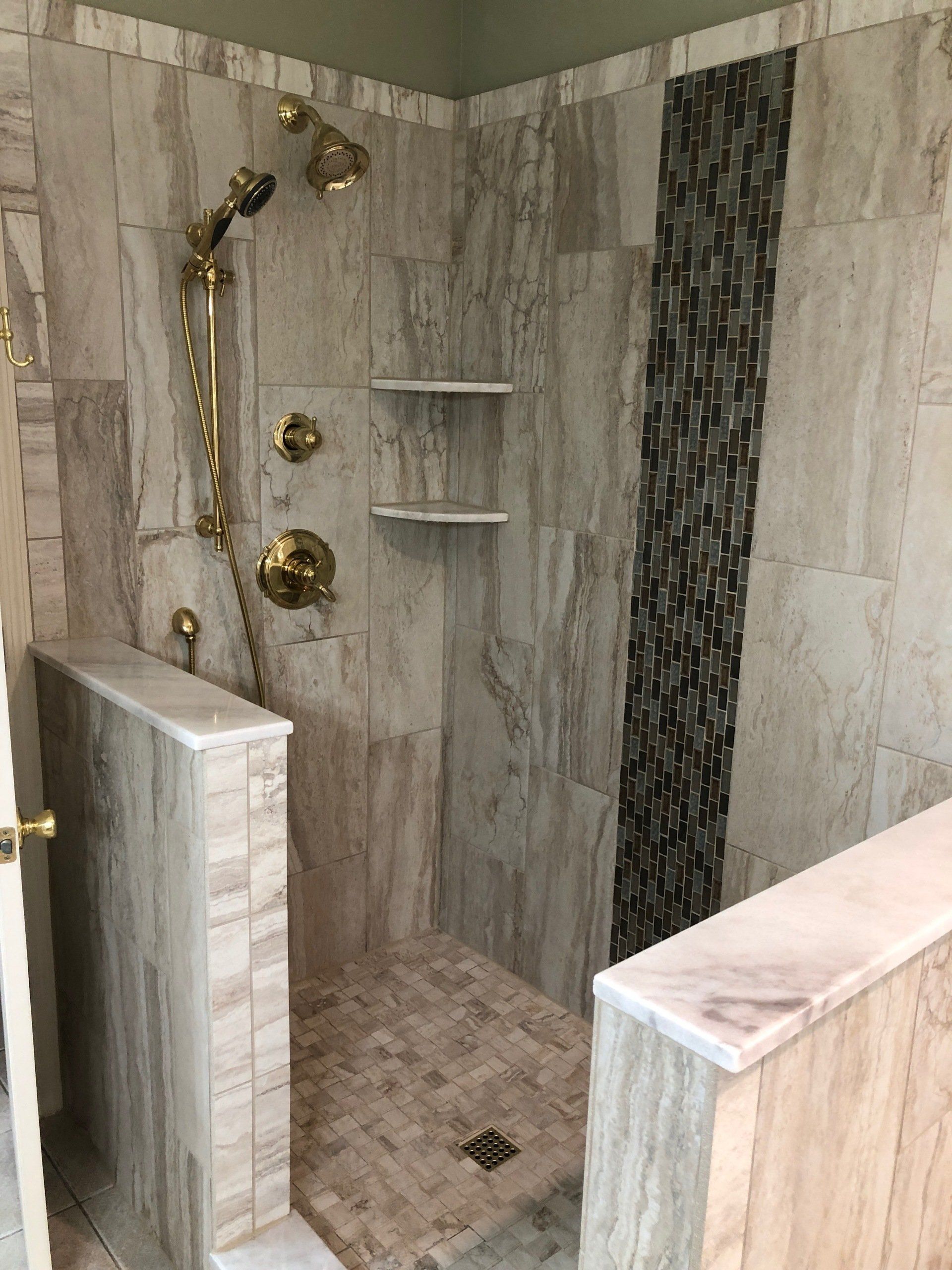 Walk-in shower with beige tile and gold fixtures; includes shelves, a mosaic accent, and low walls.