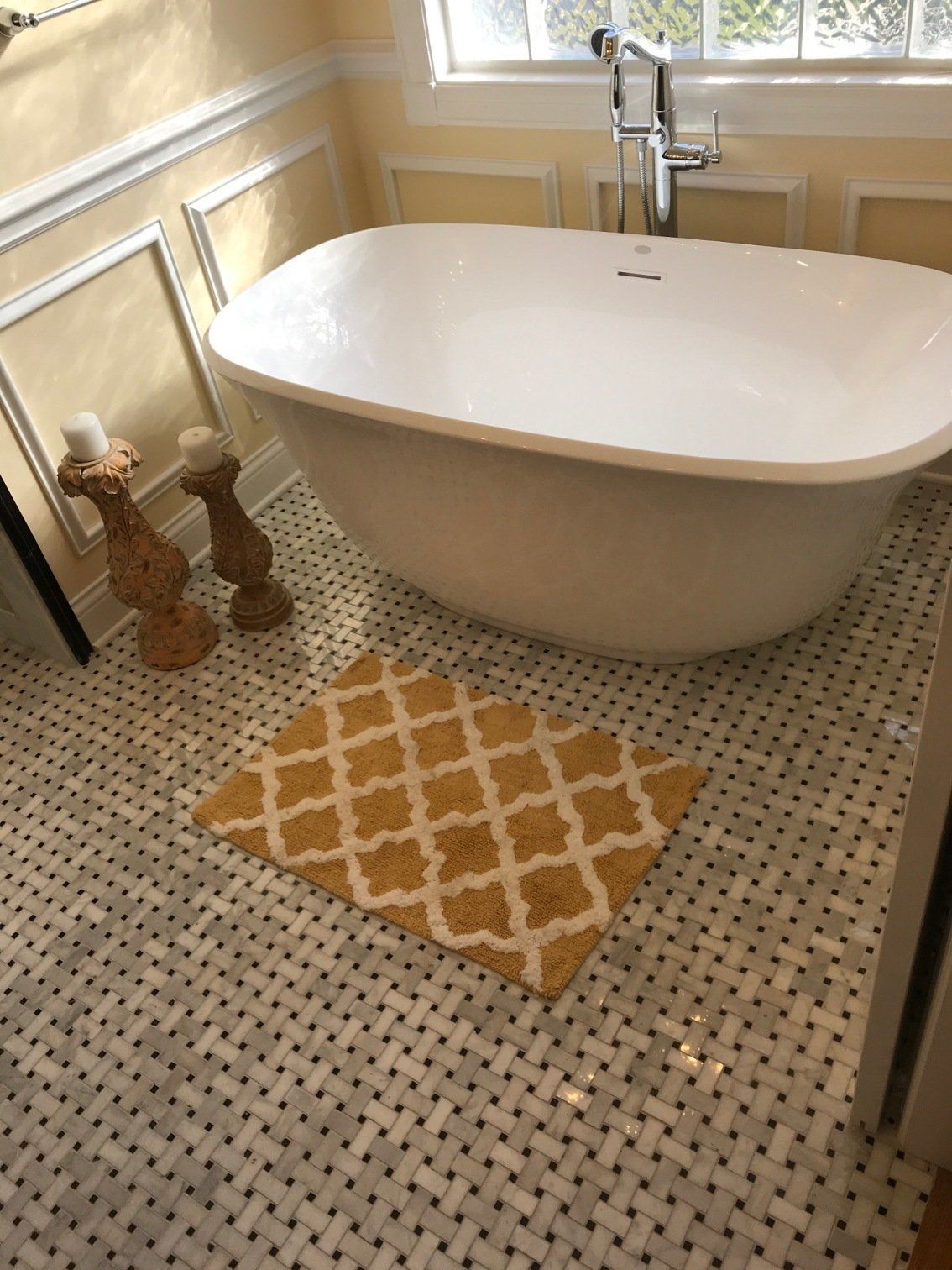 A white freestanding bathtub in a bathroom with a gold patterned rug on tiled flooring.
