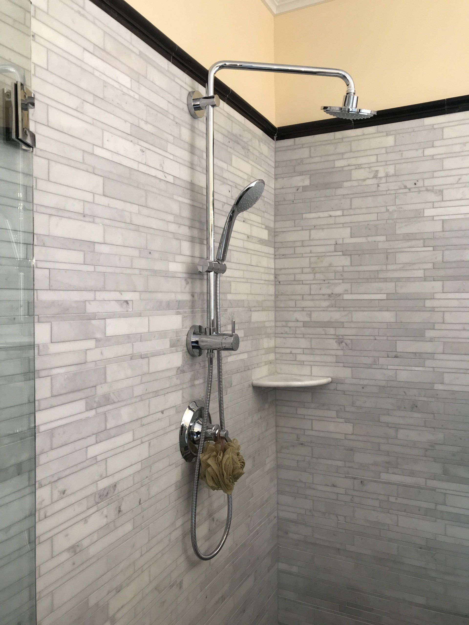 Shower with chrome fixtures against a white and gray tiled wall, including a handheld shower head.