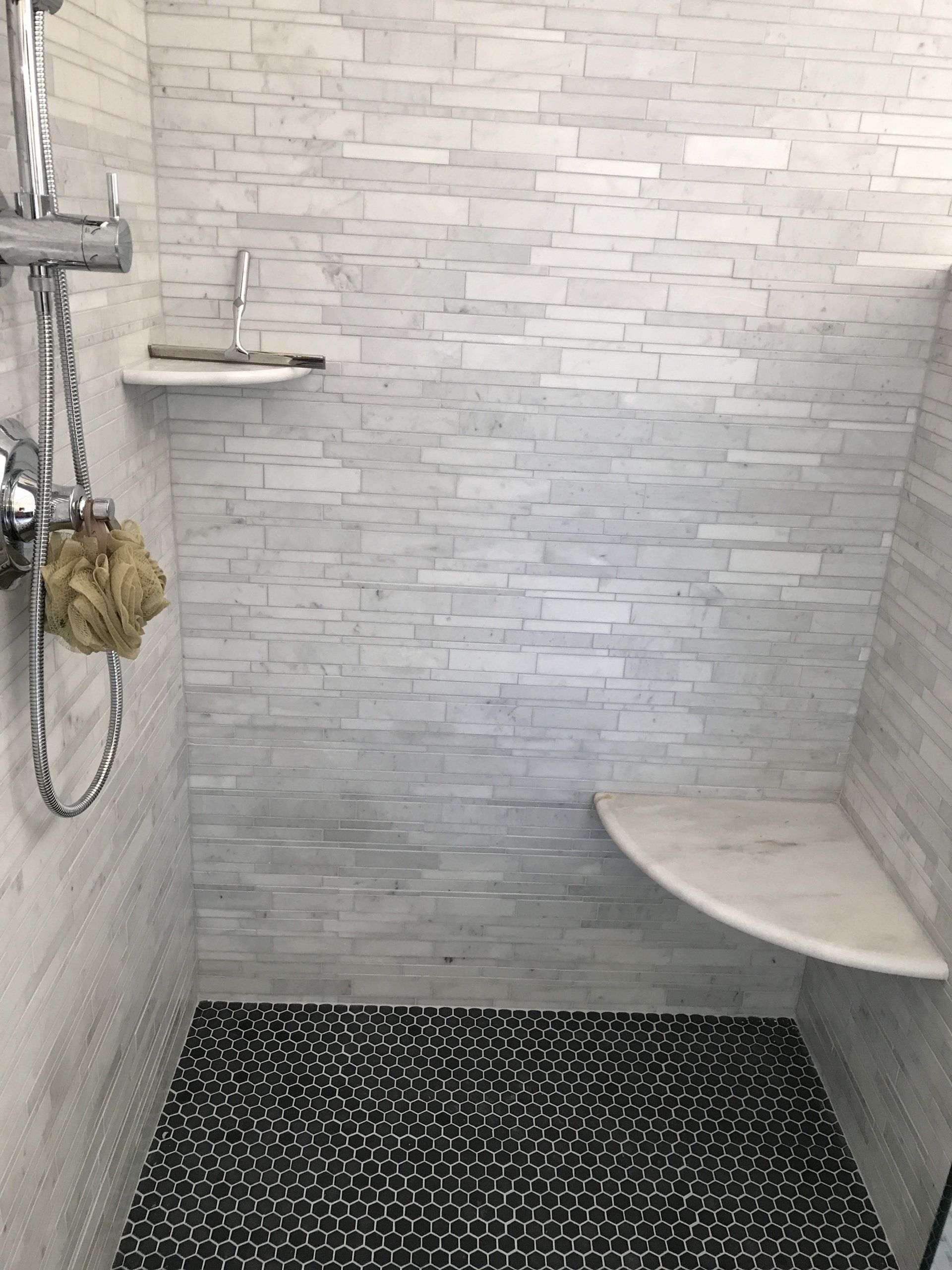 Shower with gray and white brick-like tile, with a black and white textured rug. Shelves on the wall.