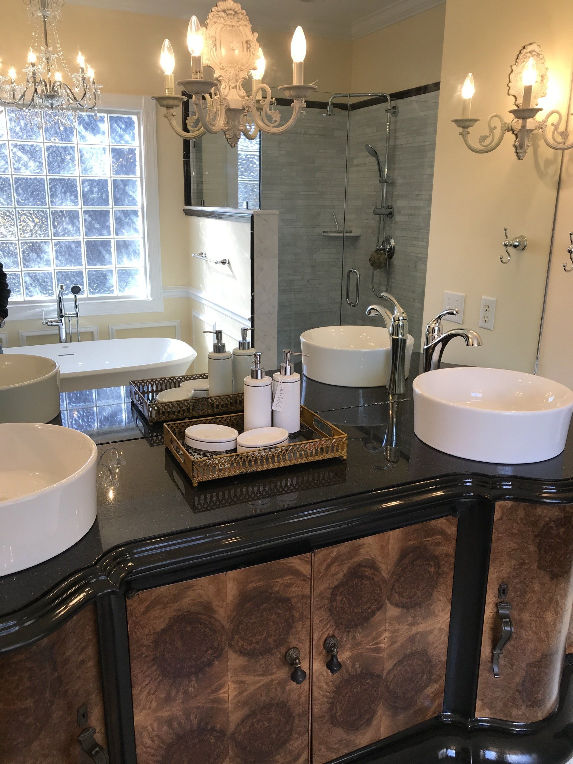 Elegant bathroom with double sinks, ornate vanity, and chandelier; a large mirror reflects the shower and a window.