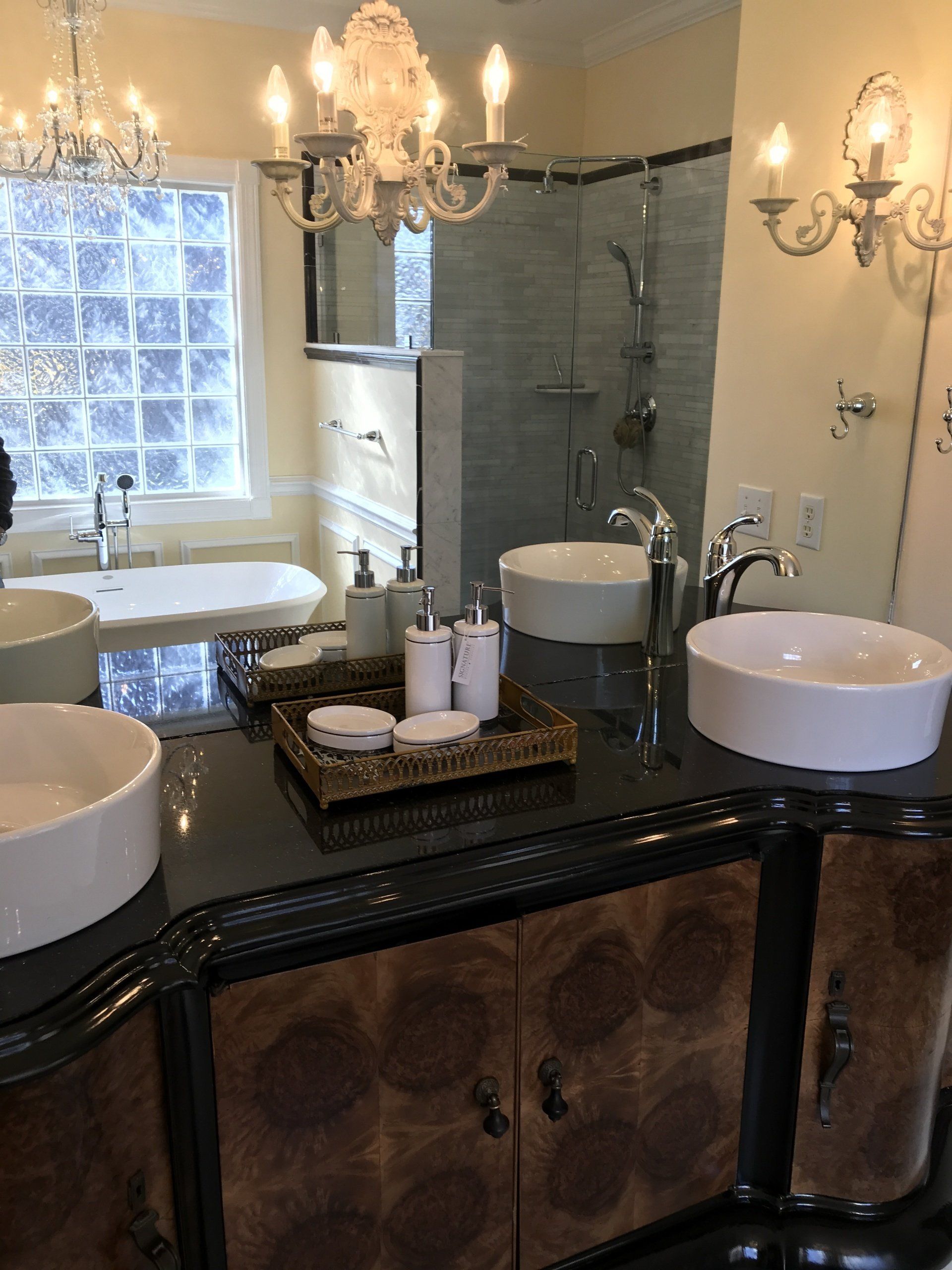 Bathroom with double sinks, a dark countertop, ornate wood cabinet, and chandelier lighting.