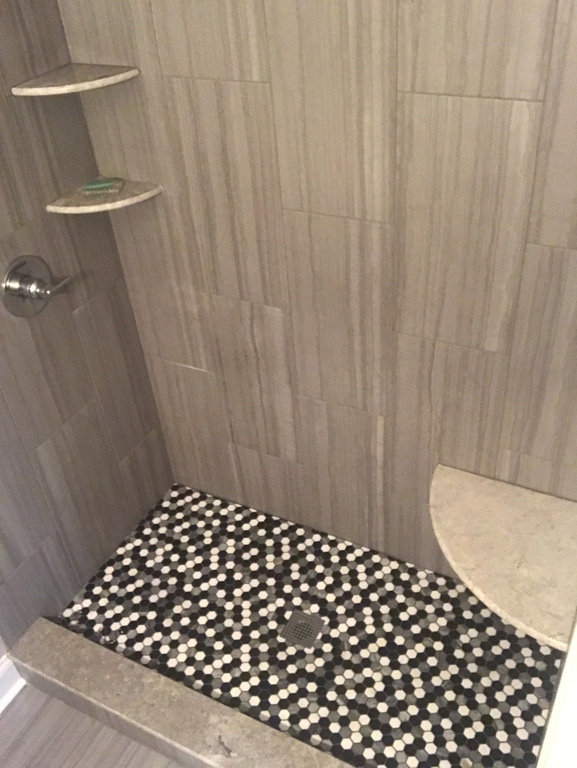 Shower with gray tiled walls and black/white pebble floor, with a built-in shelf.