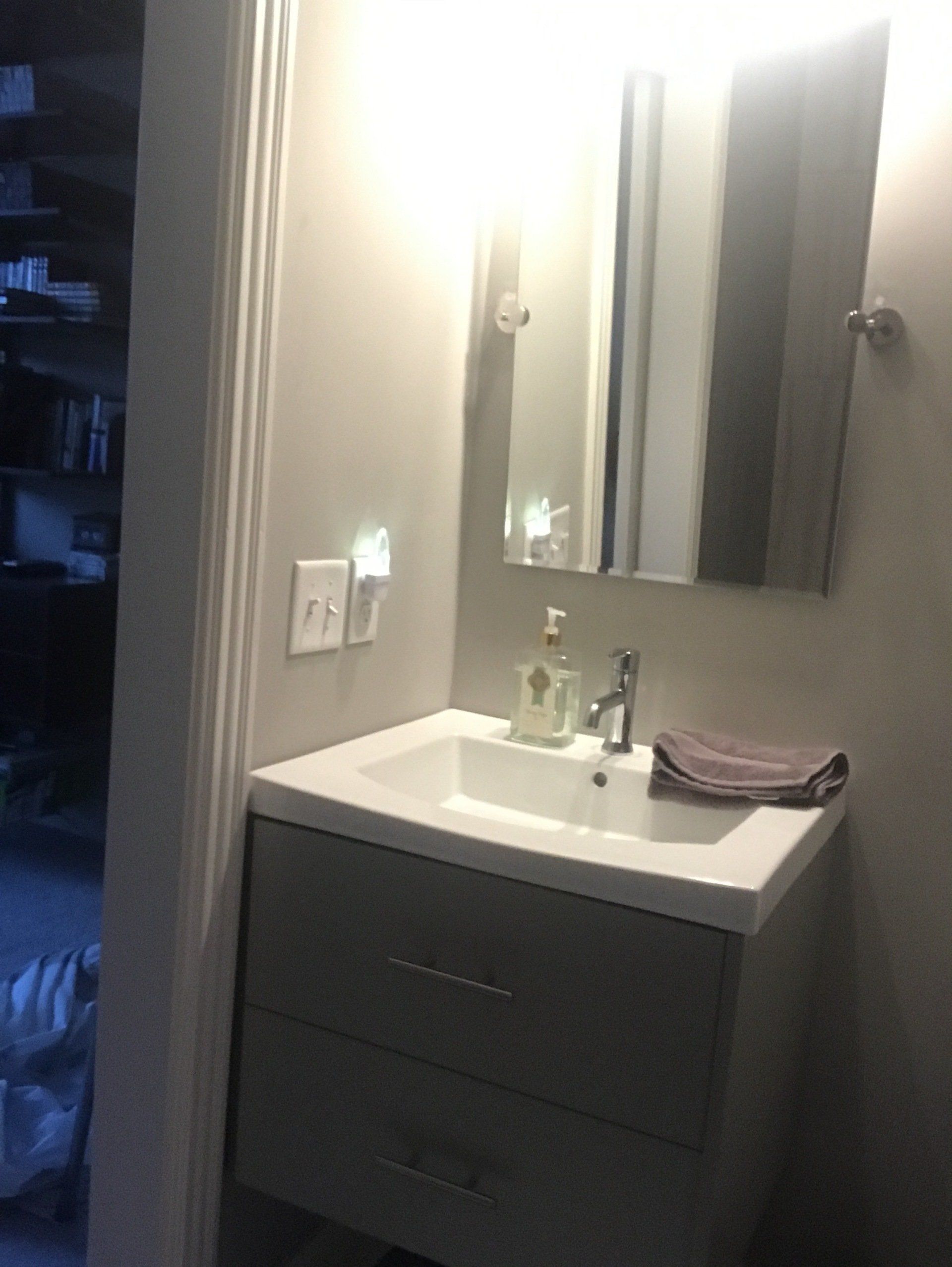 Bathroom sink with mirror, light fixture, and gray cabinet. Soap and towel on countertop.