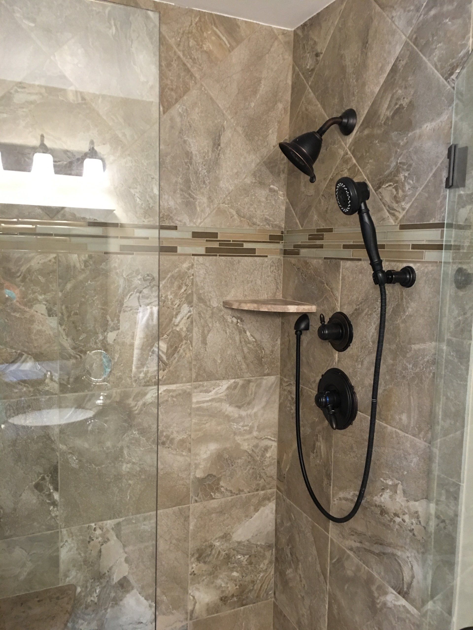 Shower with brown marble-like tiles, dark fixtures, and a glass door.