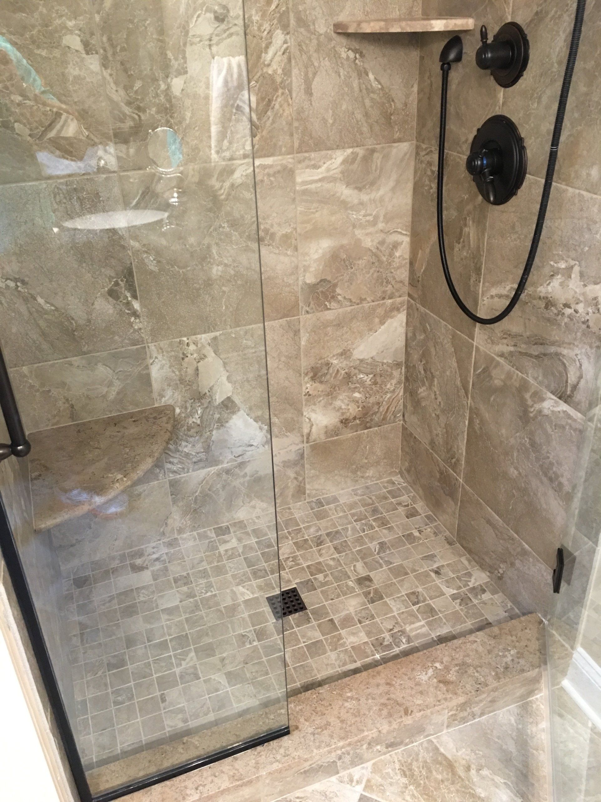 Tiled shower with glass door, dark fixtures, and a small corner shelf.