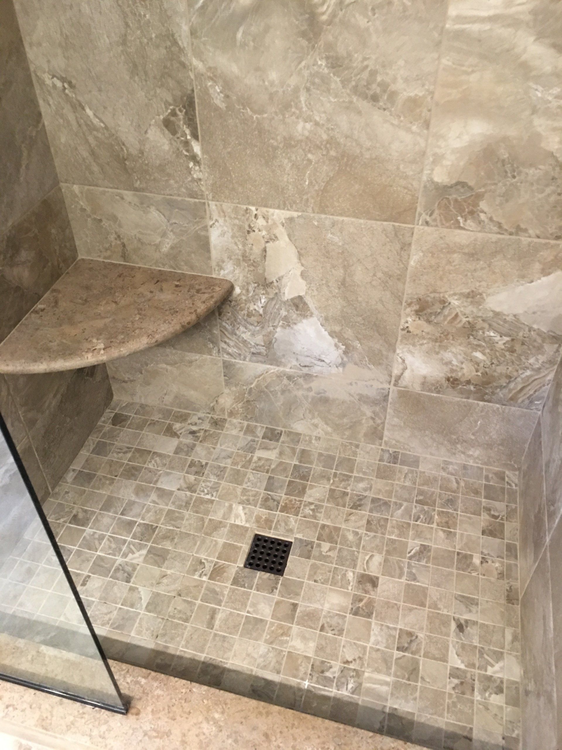 Shower with beige tiles, mosaic floor, corner shelf, and a drain.