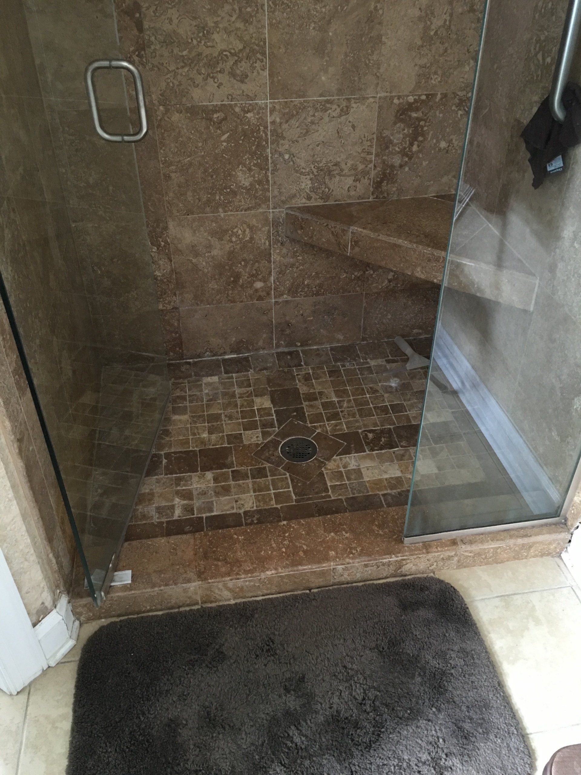 Shower with brown tile, glass door, and a dark brown bath mat.