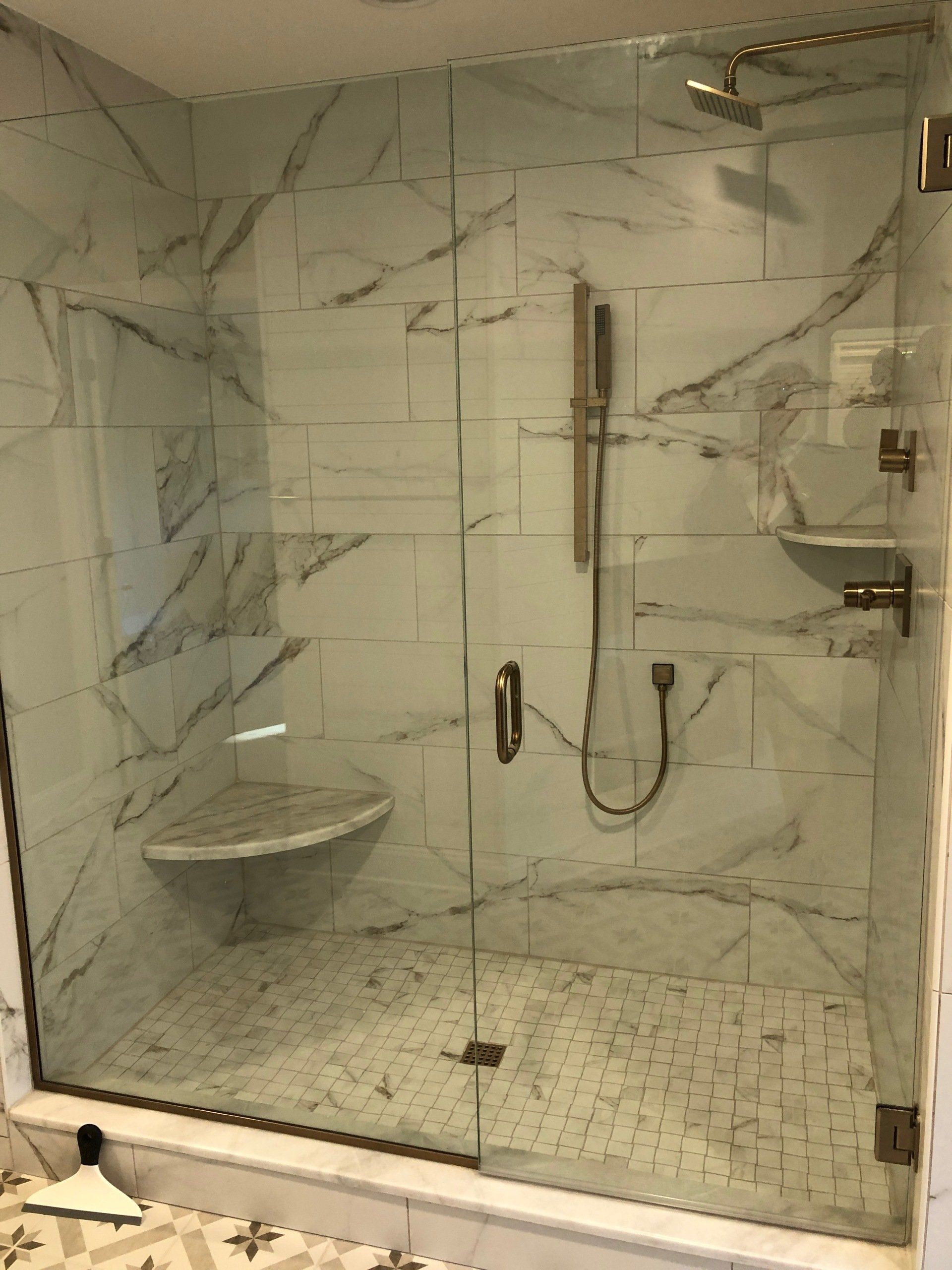 Marble-tiled shower with glass doors, handheld shower, and a built-in bench.