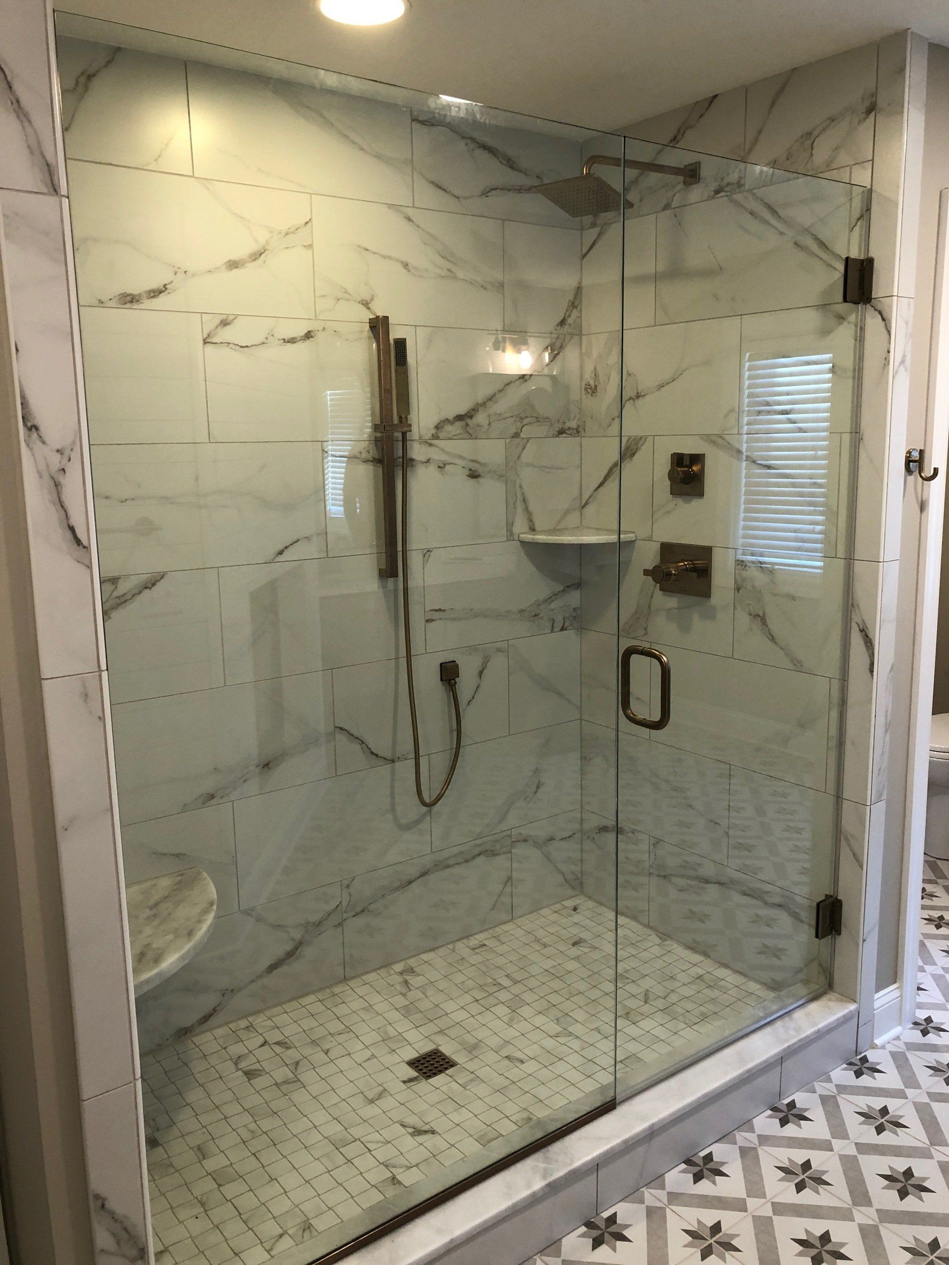 Glass shower with marble-look tile walls, white and patterned floor tiles.