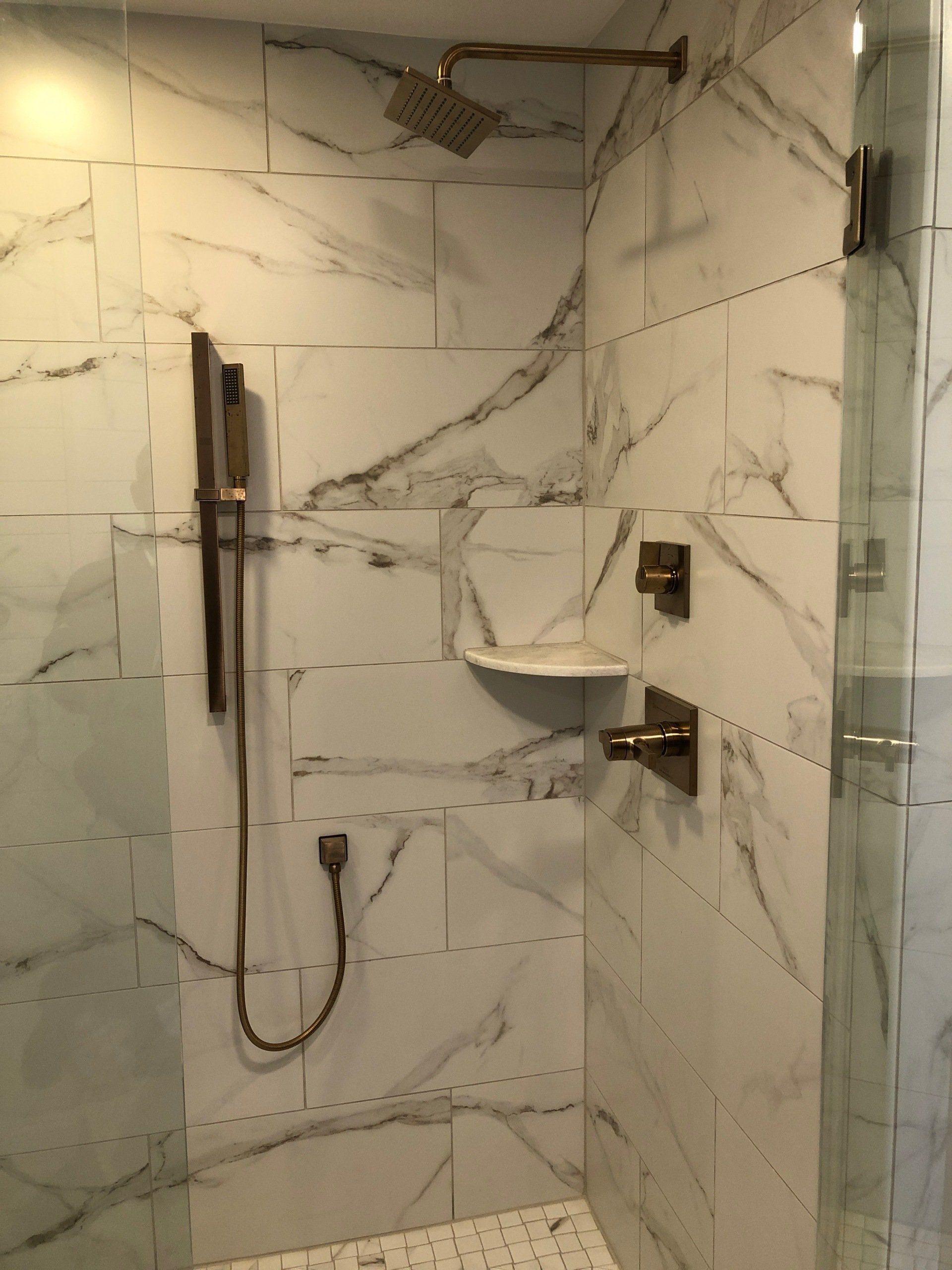 Shower with marble-look tile, gold fixtures, glass door, and built-in shelf.