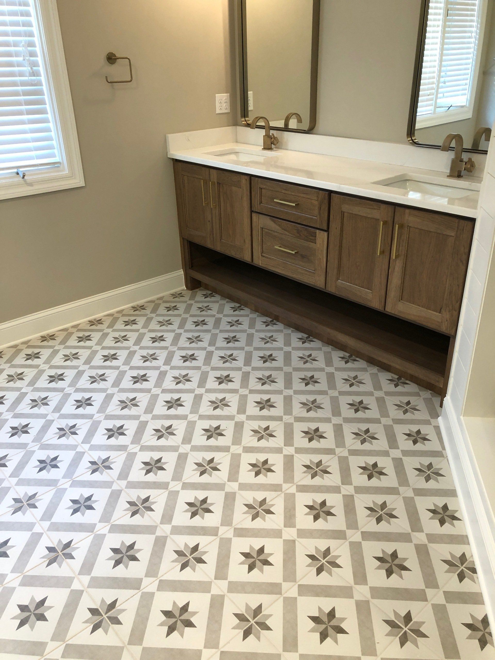 Bathroom with patterned gray and white floor, wooden vanity with white countertop and gold fixtures.