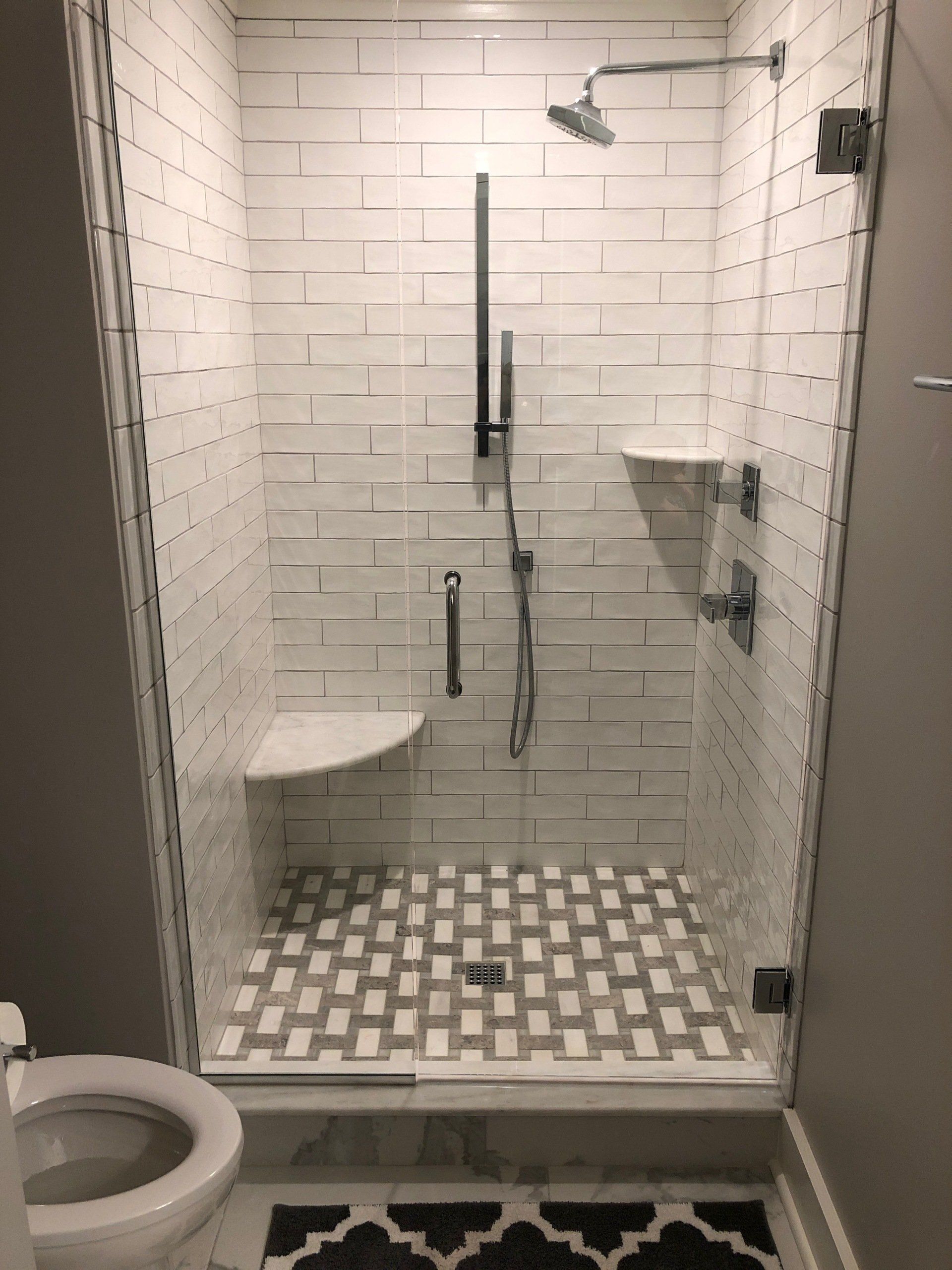 Shower with white subway tile walls, glass door, corner shelves, and patterned floor.