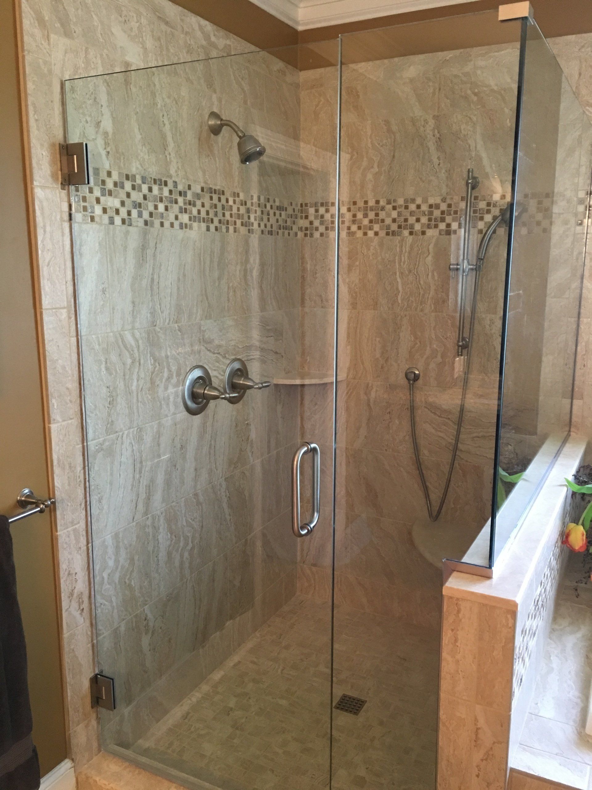 Glass shower enclosure with tan tile, chrome fixtures.