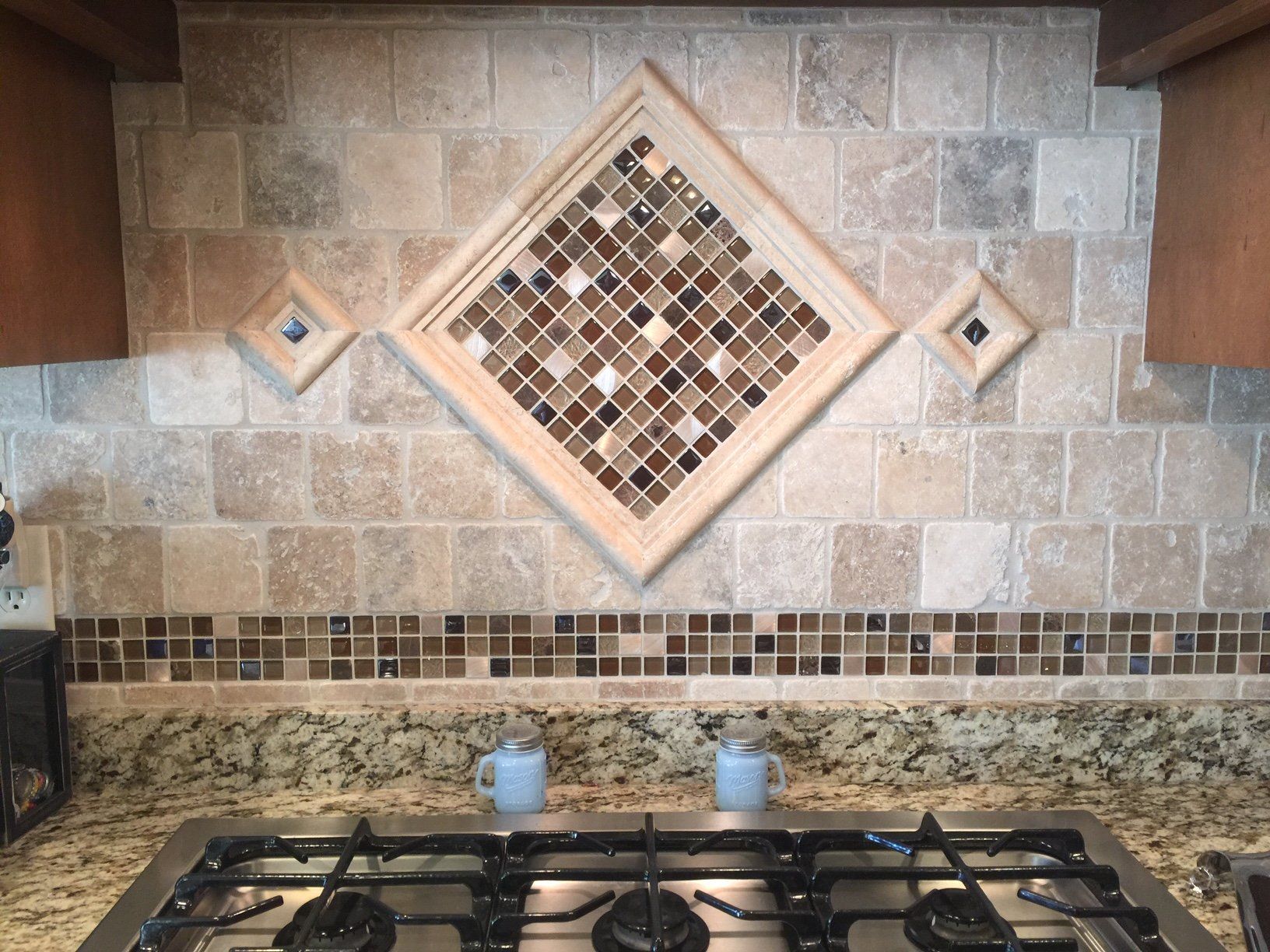Kitchen backsplash with diamond-shaped mosaic tile framed by wood, surrounded by beige and brown tile.