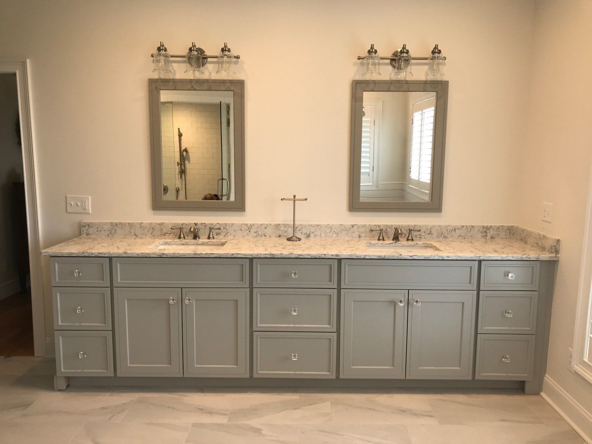 Gray double bathroom vanity with two mirrors, lights, and a speckled countertop.