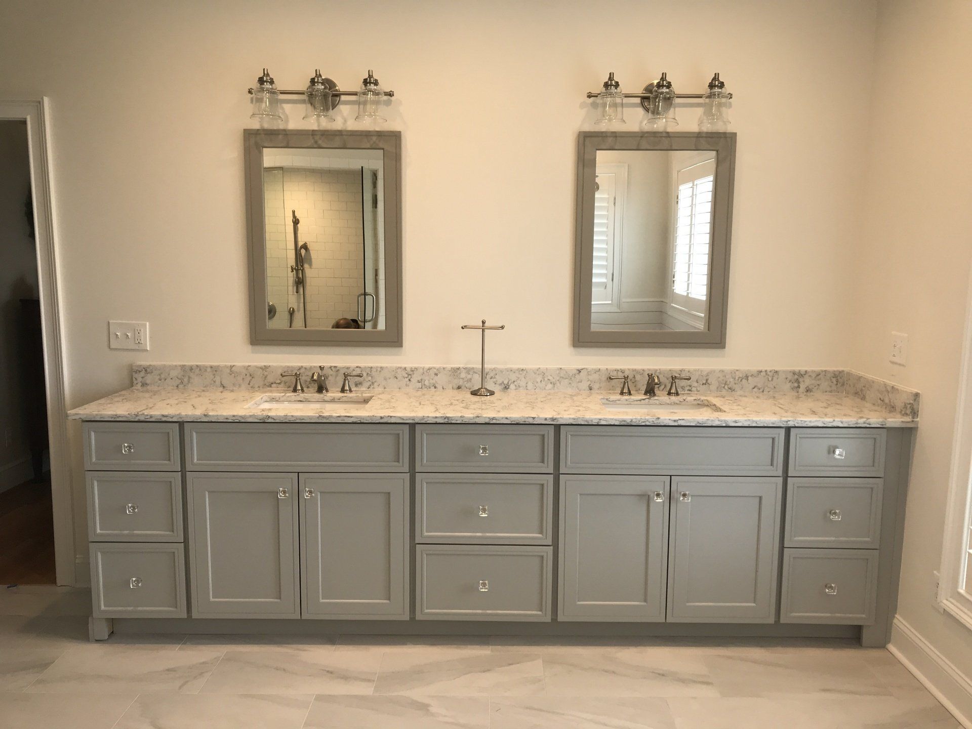 Double vanity with gray cabinets, granite countertop, and mirrors with lighting.